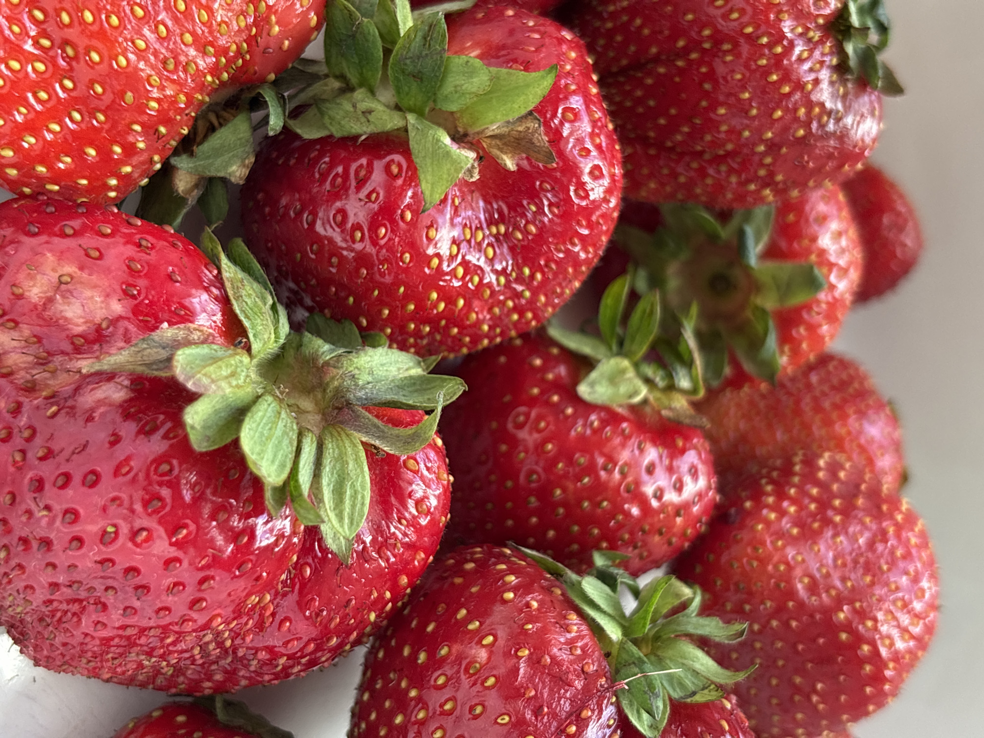 A close-up, overhead shot shows a pile of fresh, red strawberries. The berries are ripe and plump, with visible seeds and green stems. The background is a soft, neutral tone. The image does not provide any information about the city of Tallinn, Estonia, or any specific location within it. There are no people or actions depicted in the scene.