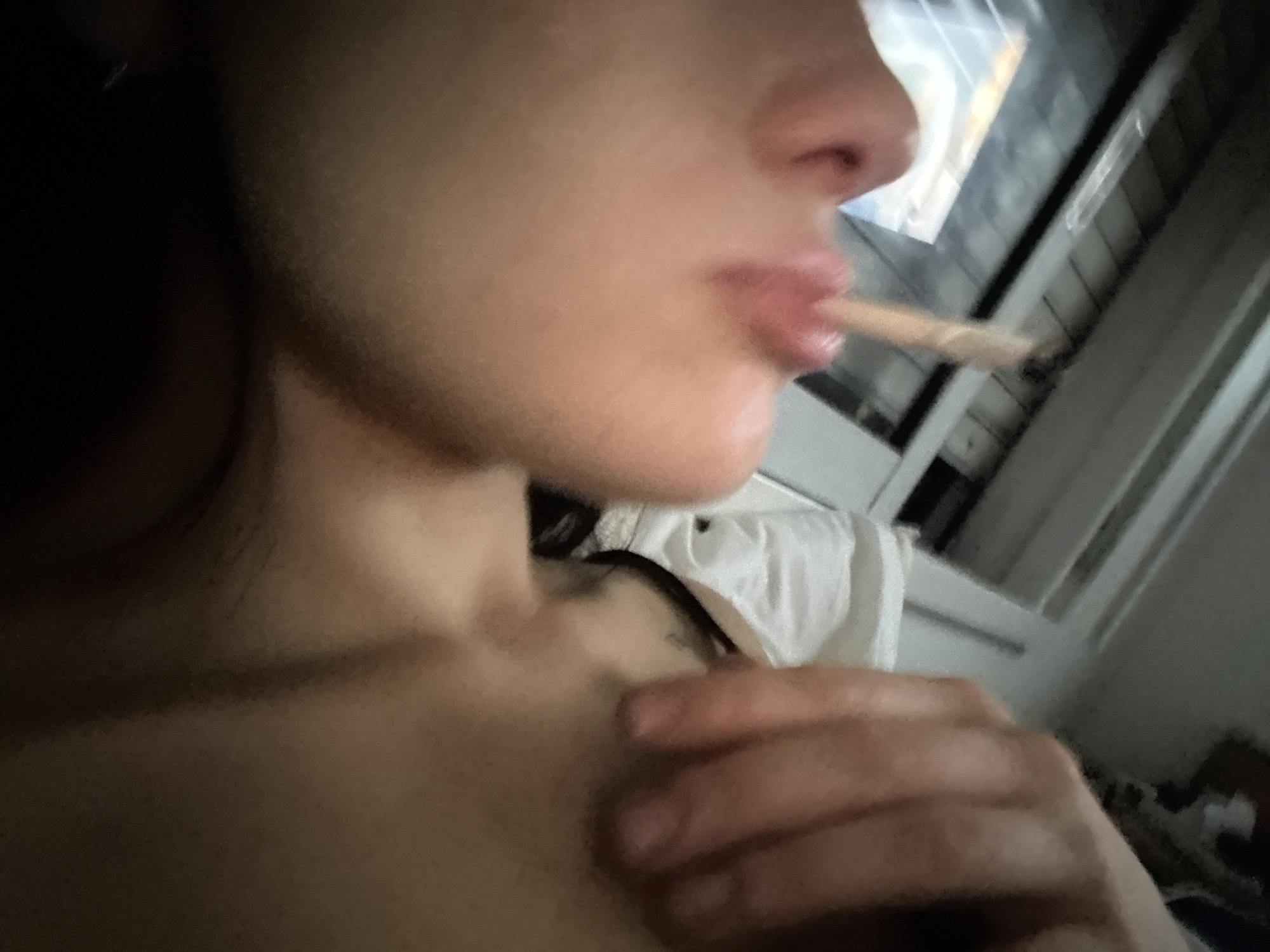 The image shows a close-up of a person's face and upper body. The person is holding a rolled cigarette or joint in their mouth. The background is blurry, but appears to be an interior space with a window. The location in the city of Buenos Aires, Argentina, cannot be determined from the image.