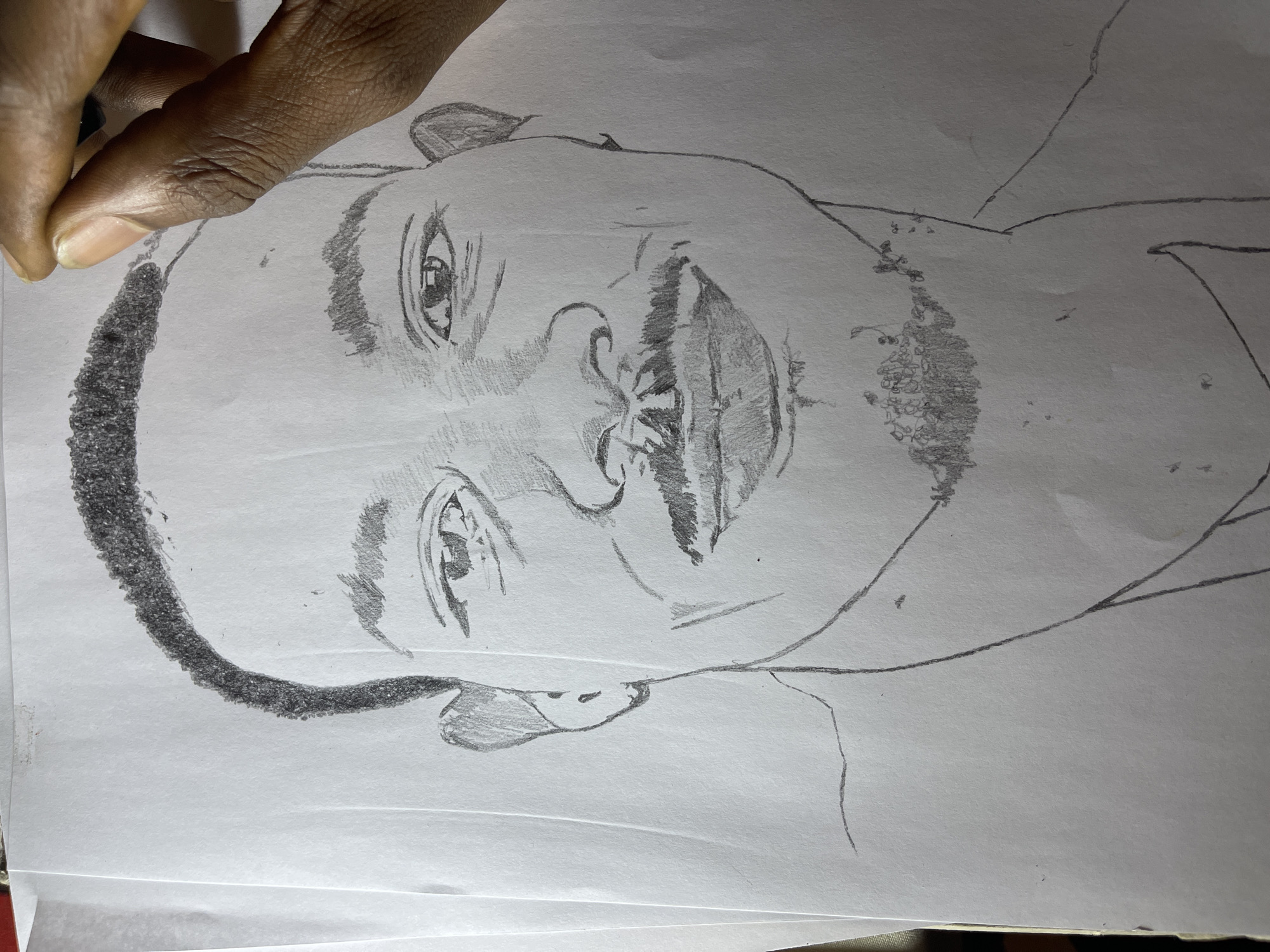 The image shows a pencil sketch of a man's face on a piece of paper. The sketch is incomplete, with some areas more detailed than others. The man has a close-cropped haircut, a mustache, and a goatee. The sketch captures the details of his eyes, nose, and mouth. A hand is visible in the upper-left corner of the image, holding the paper. The location of the sketch and the individual in the image in Jos, Nigeria is not provided in the image.