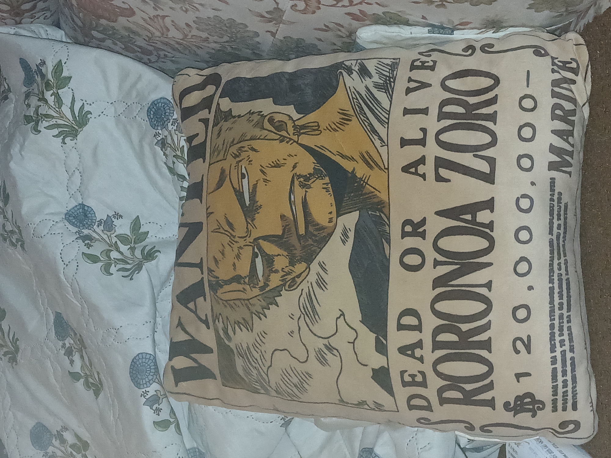 The image depicts a pillow with a "One Piece" wanted poster design, featuring the character Roronoa Zoro. The poster indicates a bounty of $1,200,000,000 and the designation "MARINE." The pillow rests on a bed with patterned bedding. No specific location in Bengaluru, India, or any people or interactions are discernible in the image.