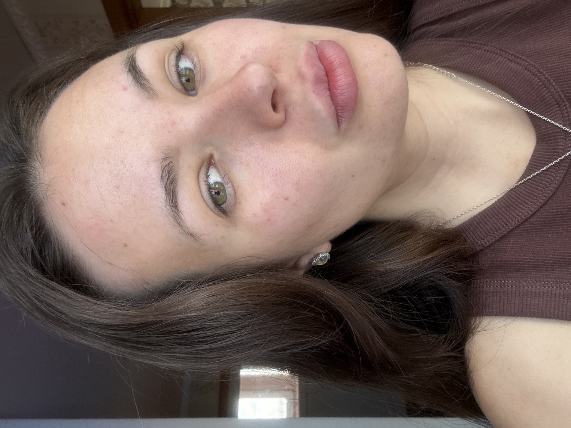 A close-up, tilted portrait of a woman with fair skin and hazel eyes. She has brown hair and a silver necklace. She is wearing a brown top and an earring is visible in her left ear. No information indicates this image was taken in Bely Yar, Russia.