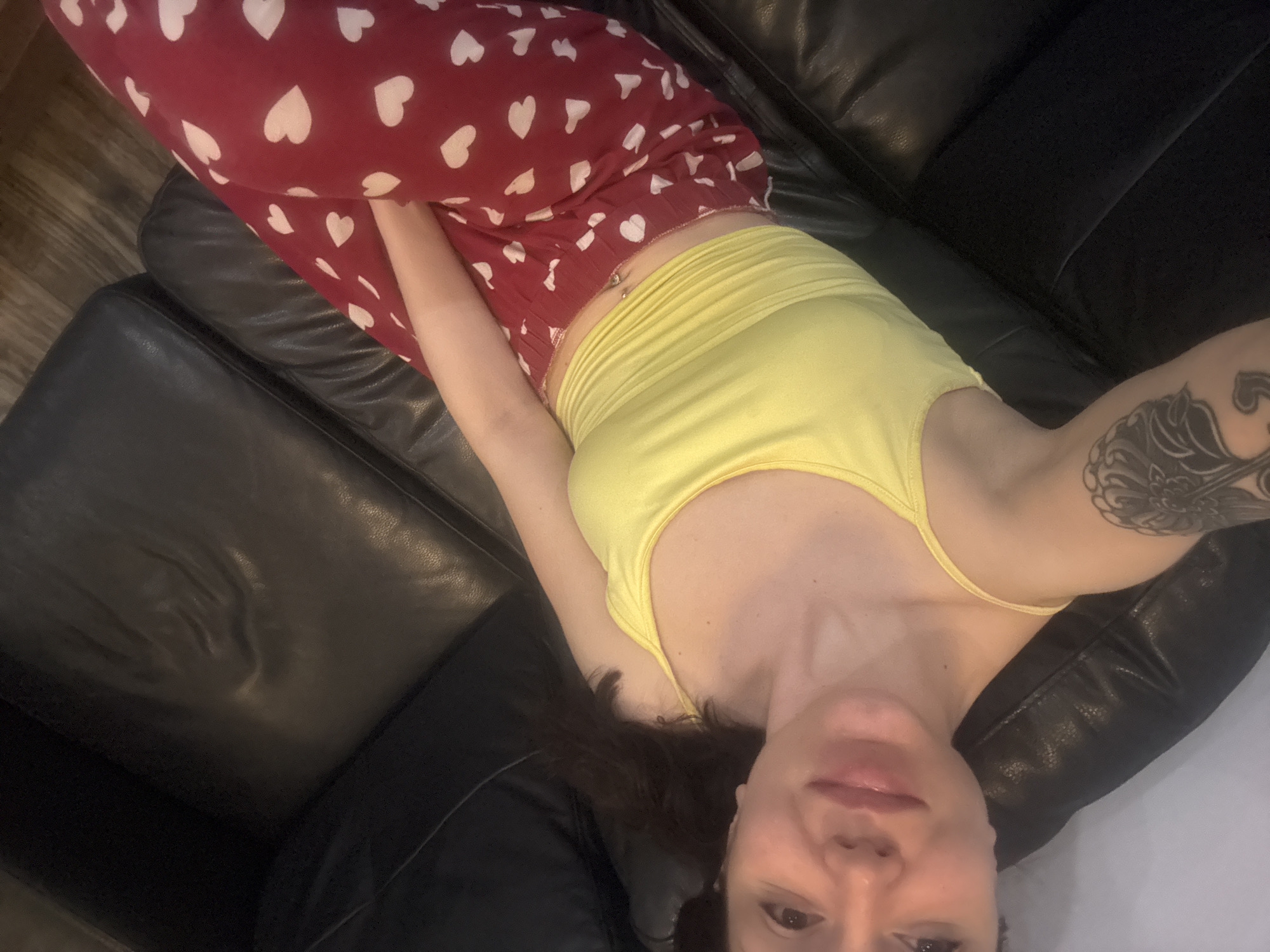 A woman is lying on a black leather couch. She is wearing red pants with white hearts and a yellow tank top. The location in Krasnovo, Bulgaria cannot be determined from this image.