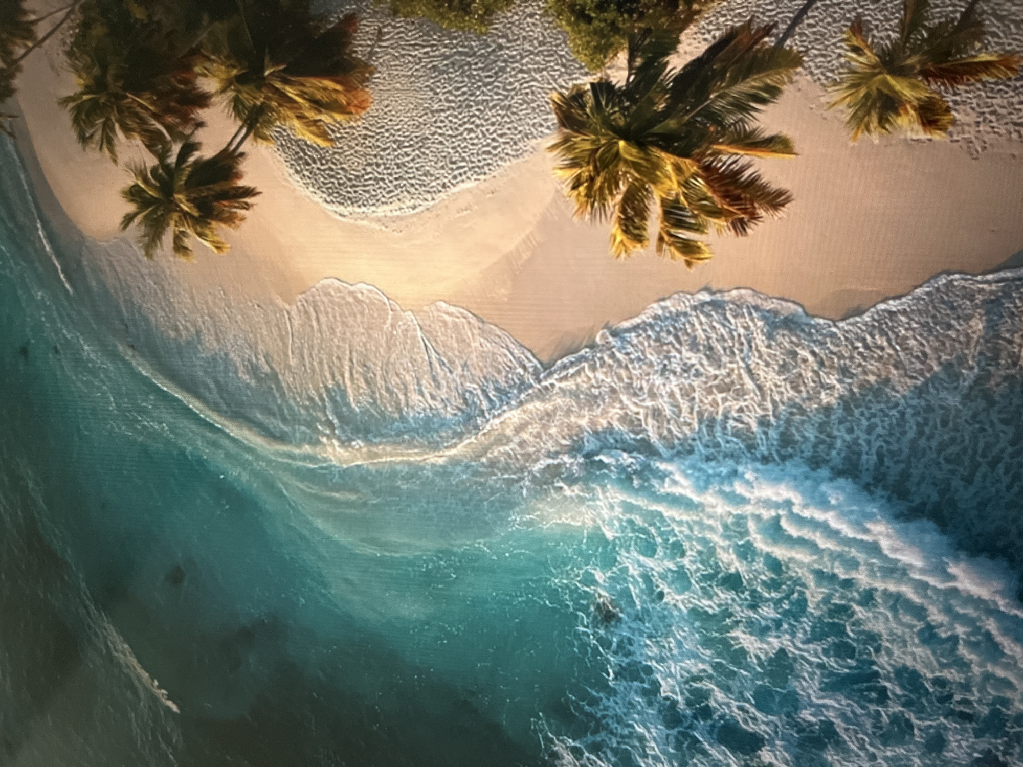 An aerial shot captures a serene tropical beach with crystal-clear turquoise water gently lapping onto a sandy shore. Palm trees with lush green fronds and golden-brown trunks dot the coastline, casting shadows on the sand. The waves create intricate patterns as they recede, leaving behind a foamy white lace along the water's edge. The scene is bathed in warm sunlight, highlighting the vibrant colors of the ocean and vegetation. The location is Unknown, Unknown.