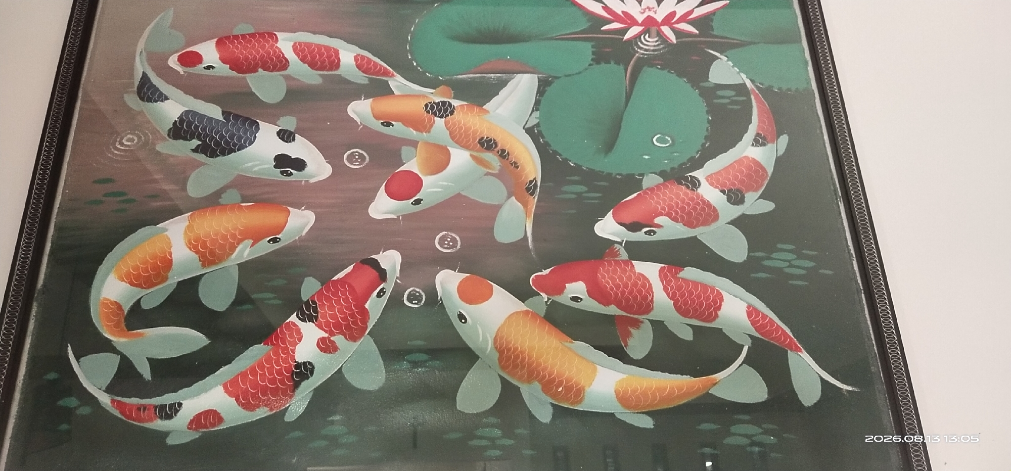 The image displays a framed artwork featuring a school of koi fish swimming in a pond. The koi fish are depicted with vibrant colors, including white, orange, red, and black markings. Some fish have distinct patterns of scales. There are also lily pads and a lotus flower visible in the background, rendered in shades of green and pink. Bubbles are scattered throughout the water. The artwork has a dark frame with a decorative border. A timestamp "2026.08.13 13:05" is visible in the lower right corner, suggesting the image was taken on this date and time. The overall scene is a still image of an artistic representation of aquatic life. The provided location information "Matabu, Indonesia" cannot be visually confirmed or inferred from the image content.