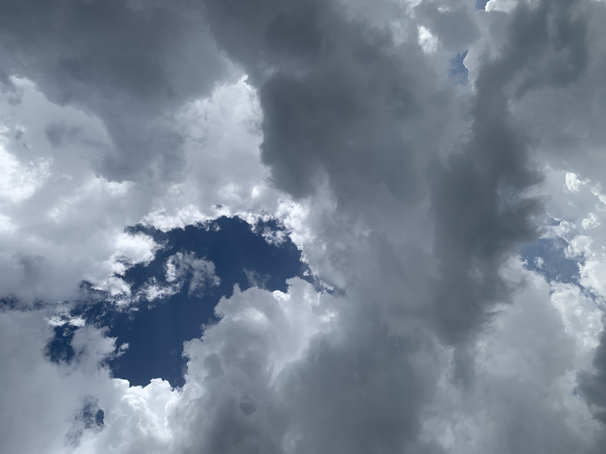 This media file depicts a dramatic sky filled with a mix of dark, heavy storm clouds and lighter, more diffused clouds. A patch of deep blue sky is visible through an opening in the clouds, suggesting a break in the weather. The lighting indicates it is daytime, likely afternoon, given the contrast between the bright white of some clouds and the deep grays and blues of others. The scene is purely atmospheric, focusing on the natural elements of the sky. There are no people, objects, or man-made structures visible. The weather appears to be unsettled, with the presence of storm clouds hinting at potential rain or a recent downpour. The image evokes a sense of power and dynamism in nature, with the shifting cloud formations creating a visually striking contrast. The lack of any specific landmarks or identifiable features makes it difficult to pinpoint a precise location beyond the general context of a sky. There is no visible text in the media file.