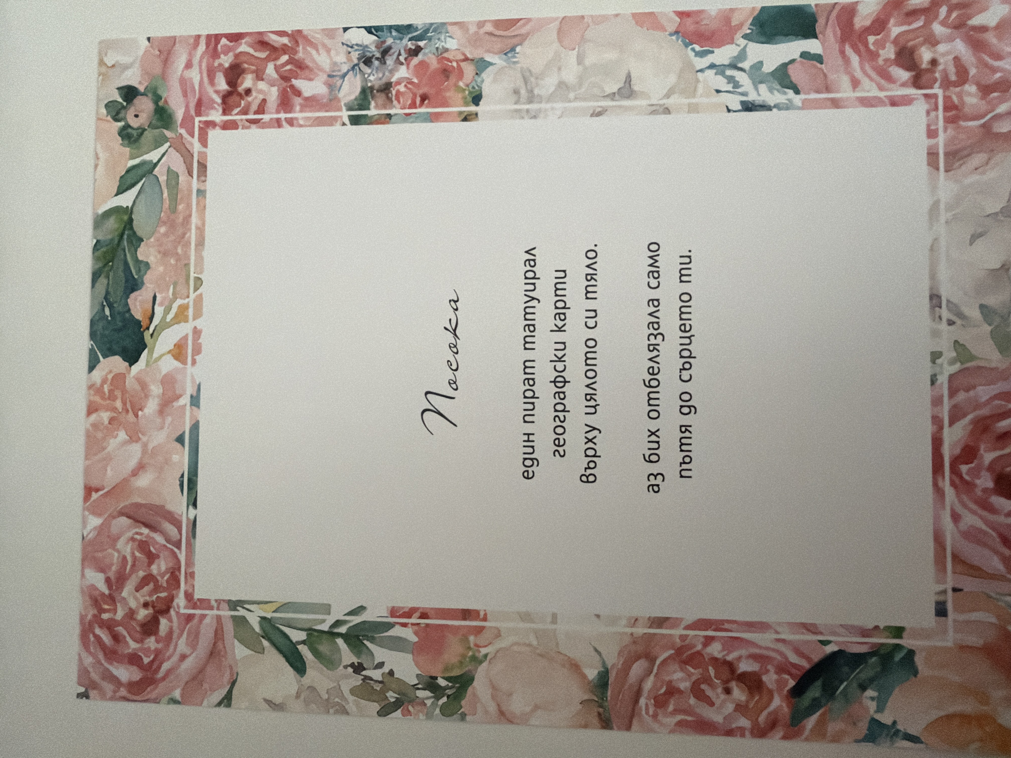 The image shows a close-up of a card with a floral border. The card contains text in Bulgarian written in a script font for the title and a standard font for the rest of the text. The text appears to be a poem or a personal message. There are no people, actions, or interactions depicted in the image. The environment is a plain white background, suggesting the card is placed on a surface. The location in Pazardzhik, Bulgaria is not discernible from the image.