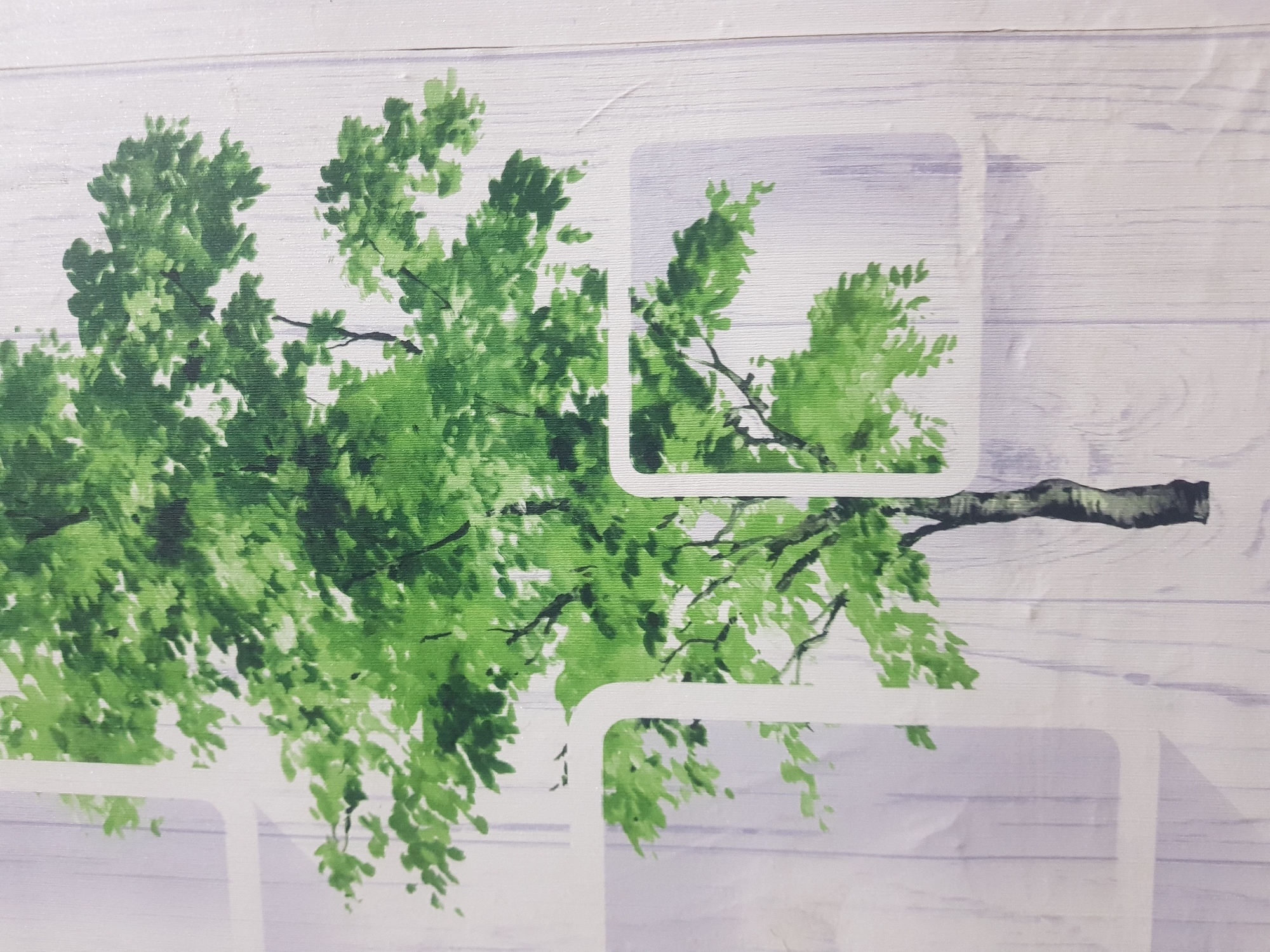 The image displays a mural of a tree with lush green foliage and a textured, wood-like background. The mural is framed by white rectangular shapes with rounded corners, suggesting it is part of a larger decorative design. The tree's trunk is dark and textured, with branches extending upwards and outwards, covered in a dense canopy of green leaves. The background depicts a pattern of vertical light purple and white lines, resembling wood grain. The overall aesthetic is natural and somewhat stylized. The location is unknown.