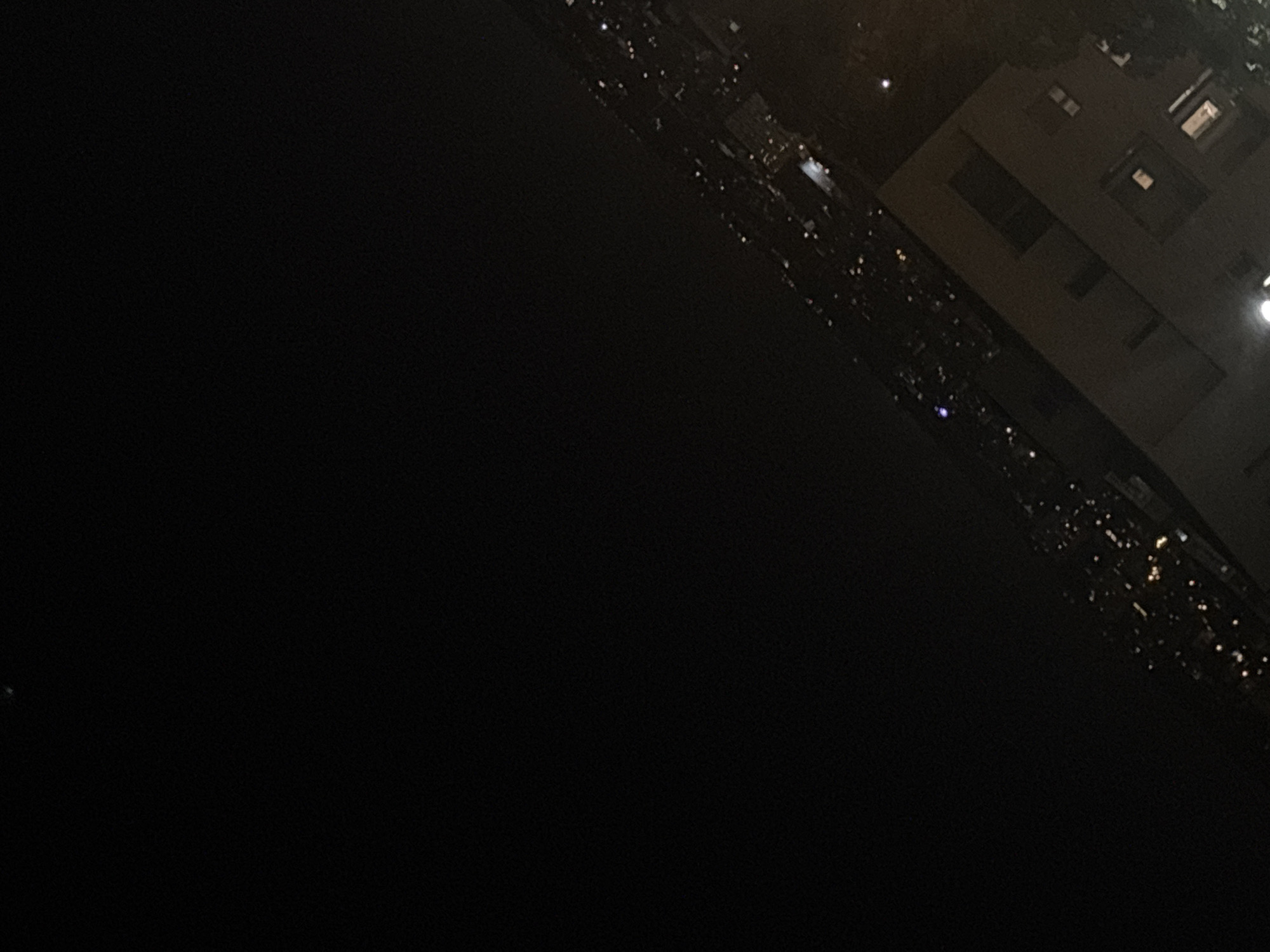 The image appears to be a nighttime view of a city from a high vantage point, possibly a building or hill. The city has many lights, which stretch into the distance. There is also a large dark area, likely water or unlit land, in the foreground. A large building is on the right-hand side of the image. It is believed to be a building in Belgrade, Serbia.
