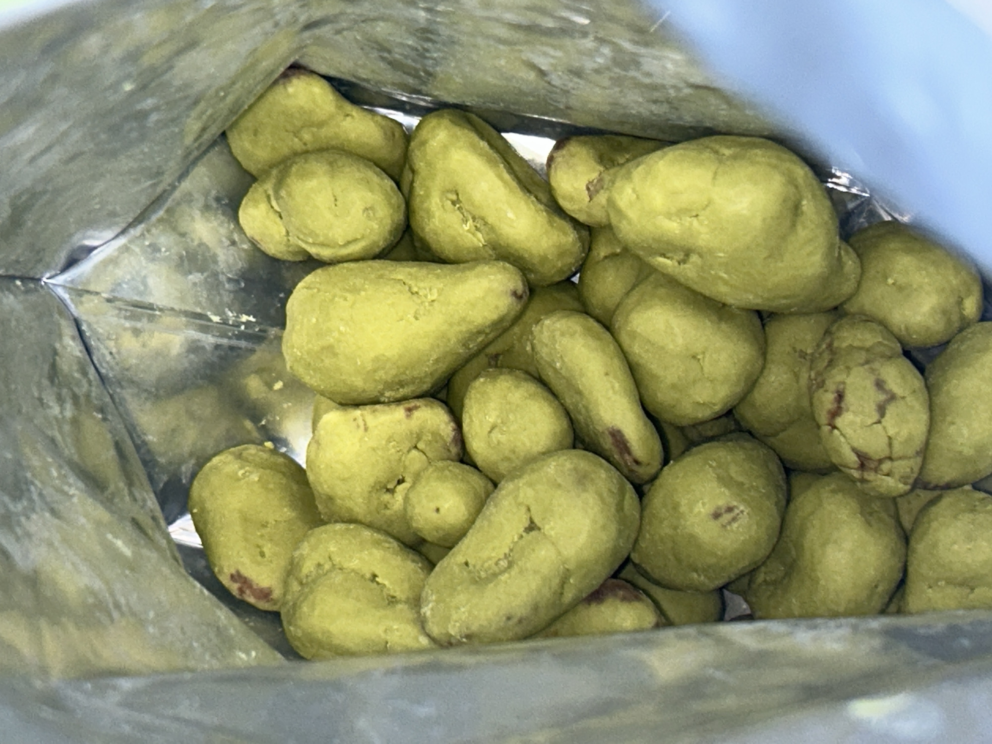 A close-up, indoor, overhead shot shows a pile of bright green, irregularly shaped candies, possibly coated peanuts or similar snacks, filling a silver bag. The candies are clustered together, with some overlapping and others partially obscured. The interior of the bag is visible, reflecting light. No people or activities are depicted. The scene is forensic and matter-of-fact, focusing solely on the visual elements of the objects within the bag. The location in Everett, United States of America, is not visually represented in the image and cannot be determined from the visual information provided.