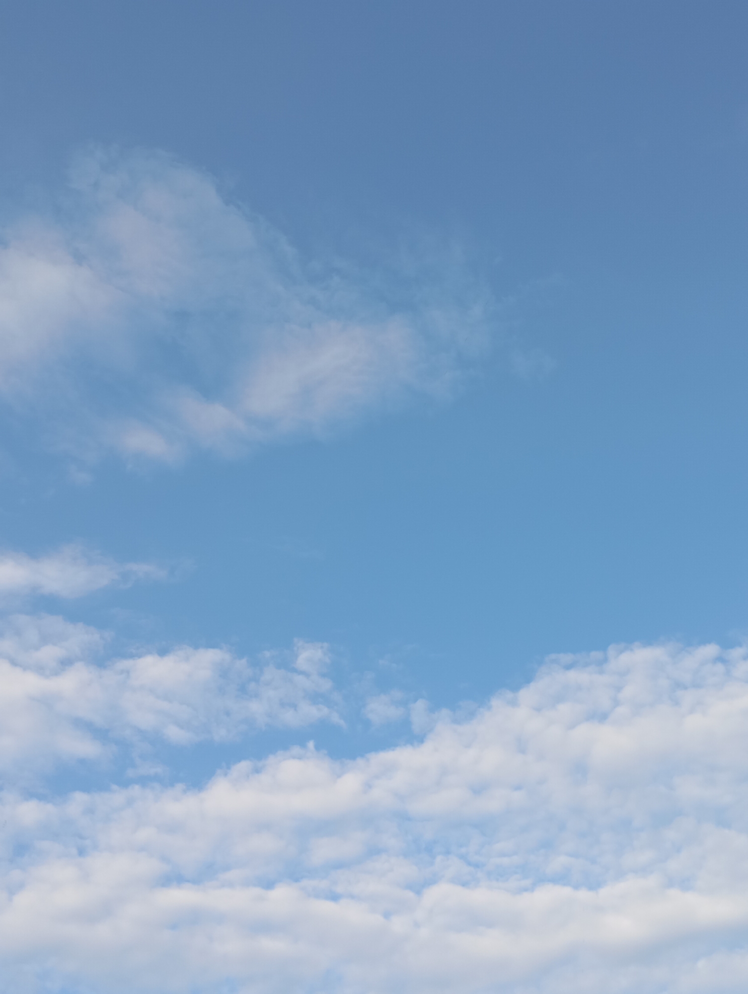 The image is a vertical, medium shot of a blue sky with scattered white clouds. The clouds are fluffy and appear to be of varying sizes, with some larger formations towards the bottom and thinner wisps higher up. The sky is a clear, bright blue, suggesting a daytime scene with good weather. There are no visible landmarks, buildings, or people in the frame. The scene is consistent with an outdoor environment, specifically an open sky view, which could be observed from anywhere, including the city of Фоки, Russia.