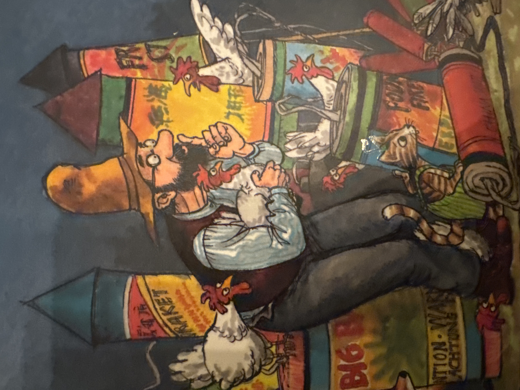 The illustration depicts a man with a beard, glasses, and a tall, conical hat standing amidst a collection of fireworks and chickens. He is wearing a blue shirt, a dark vest, and gray pants. The man is holding a chicken in his arms and gesturing with his right hand. Several other chickens are perched on or near him, and some are peeking out of large firework containers. The fireworks vary in size and color, with labels that are partially obscured but suggest they are explosives. In the foreground, a tabby cat wearing a green vest is looking towards the man. Also in the foreground, there are several large, red, cylindrical objects that appear to be firecrackers, some with fuses. The background is dark, suggesting nighttime. There is no identifiable location or city indicated in the image.