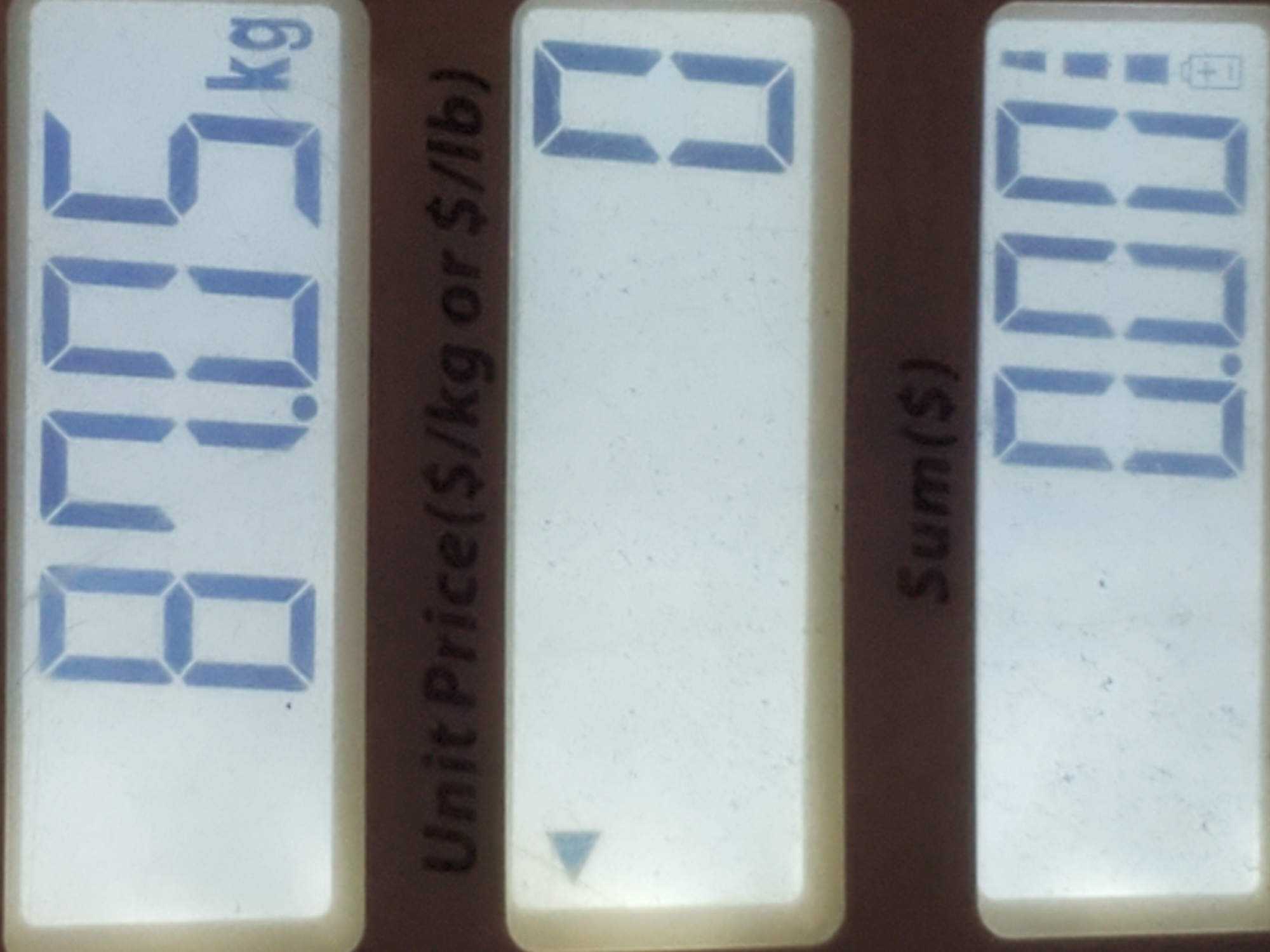 The image shows a digital scale display with three readouts. The top readout displays "87.05 kg". Below this, the text "Unit Price($/kg or $/lb)" is visible, followed by an empty display area with a small blue triangle on the left. The bottom readout displays "Sum($)" and then shows "0.00" with a battery icon on the right side. The scale is likely in a commercial setting, perhaps a grocery store or market.