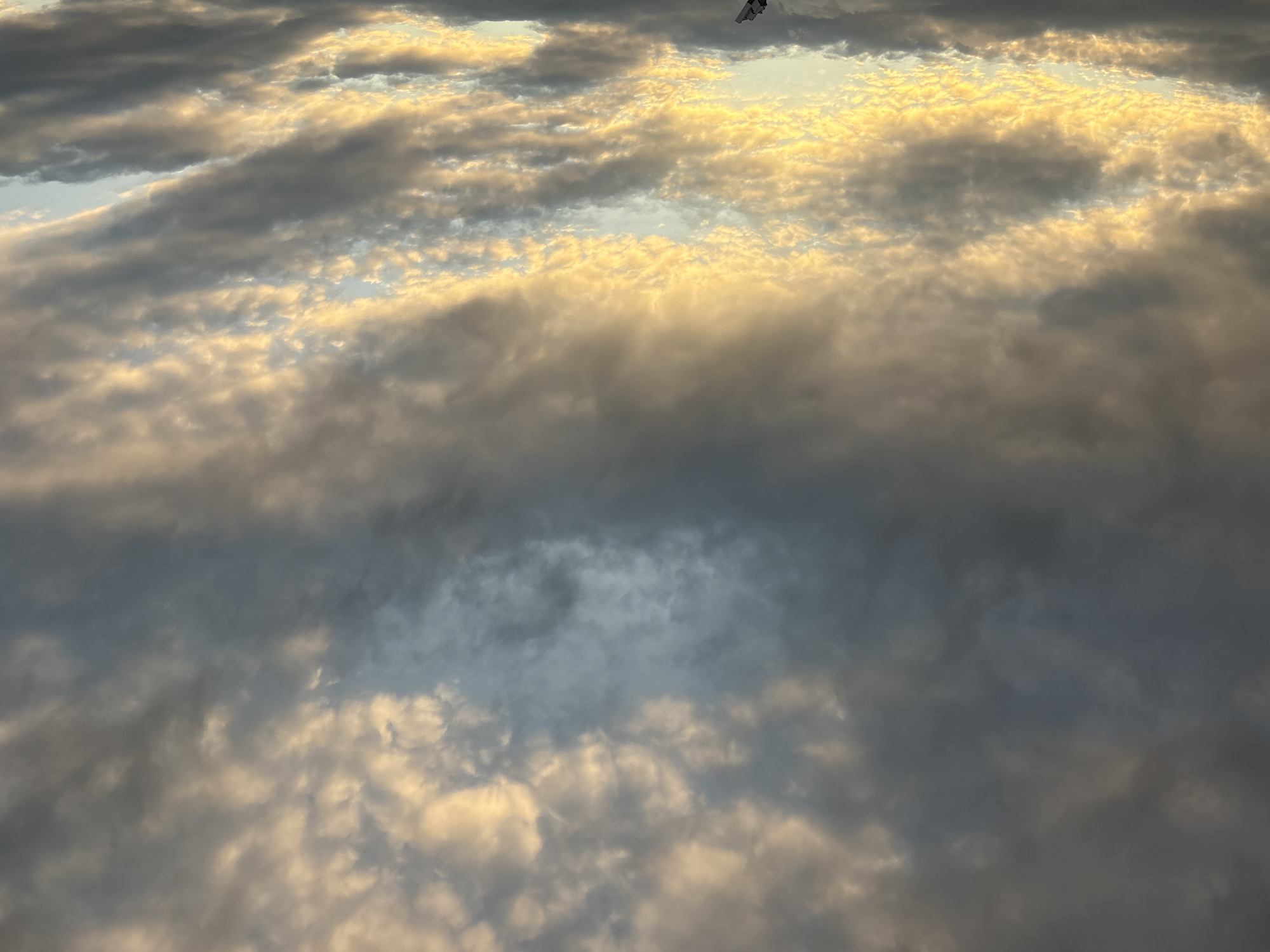 The image displays a dramatic sky filled with a mixture of dark gray and bright yellow-orange clouds. The clouds are textured and appear to be illuminated by a low-lying sun, possibly at sunrise or sunset. In the bottom center of the image, a dark silhouette of what appears to be a construction crane is visible against the brighter parts of the sky. The scene is devoid of any people or immediate human activity, with the focus solely on the atmospheric conditions and the industrial structure. The city of Georgiyevsk, Russia, is not discernible from this image; it is an abstract depiction of the sky with a single man-made object.