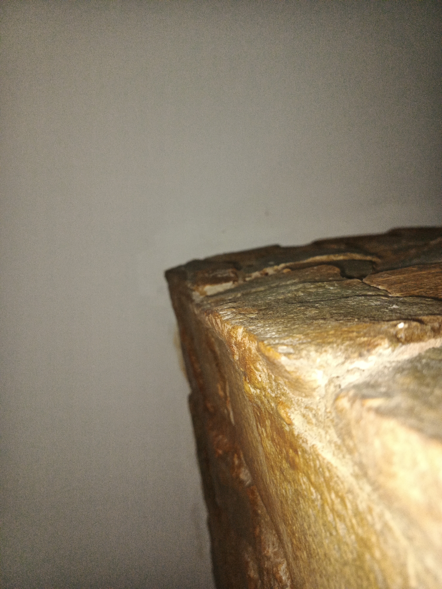A close-up shot shows the corner of a wall or structure made of layered stone or slate. The stone is predominantly brown and tan, with variations in color and texture. The wall behind the stone structure is a plain, light color, possibly white or off-white. The image has limited depth of field, blurring the background. The setting is indoors, likely under artificial lighting. There are no people, subjects, objects, actions, or interactions visible. There is no information available about the city of Los Robles, Venezuela.