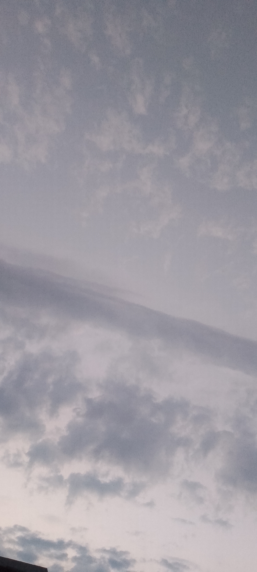 The image shows a cloudy sky over the city of Belgorod, Russia. The clouds are a mix of gray and white, with some areas appearing darker and denser than others. The sky is overcast, suggesting it may be a gloomy or rainy day. The lower portion of the image shows the edge of a building or structure, indicating an urban setting.