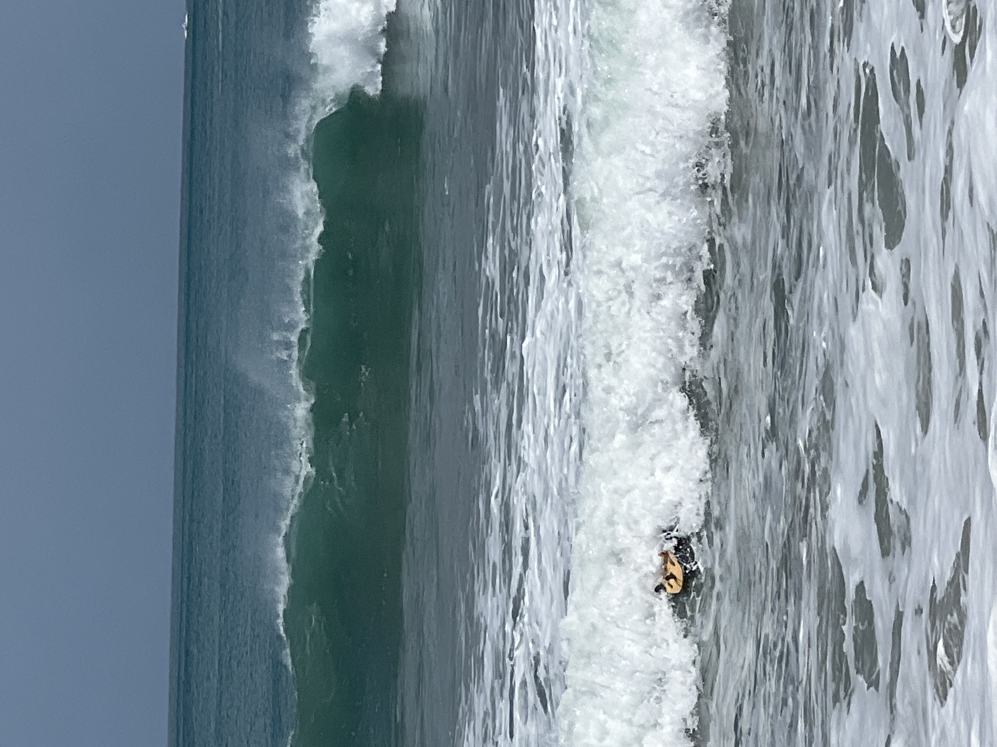A person is lying on a bodyboard in the ocean in Kuta, Indonesia. The person appears to be enjoying the waves as they crash around them. The water is a beautiful turquoise color, and the sky is a clear blue. The scene is idyllic and peaceful.