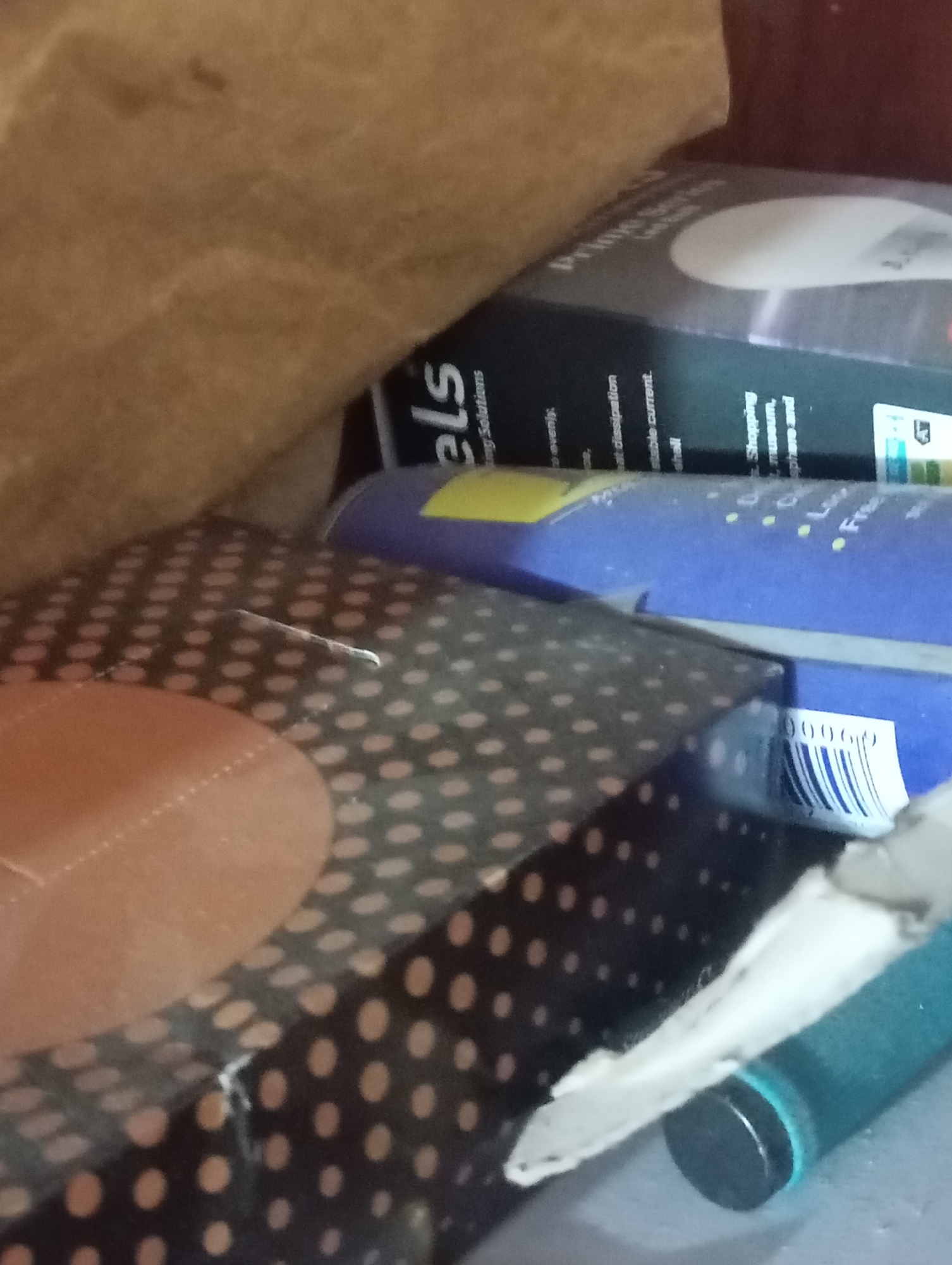 This media file depicts a close-up, indoor scene with several objects. The primary focus appears to be on packaging and electronic components, suggesting a retail or storage environment.
In the foreground, a black and polka-dotted surface with some brown circular shapes is visible, possibly part of a box or container. To the right, a bright blue object is present, with some text and what appears to be a barcode sticker that reads "00060". Above this, a dark-colored box or packaging is seen, with the word "els" prominently displayed in white text. Further in the background, a brown, textured material, possibly paper or fabric, fills the upper left portion of the frame.
The lighting is dim, and there are no clear indicators of the time of day, weather, or specific location beyond the provided context of Mansehra, Pakistan. The scene lacks any human subjects, and the focus is solely on the arrangement of inanimate objects. There are no discernible emotions conveyed due to the absence of people.
Visible text includes "els" and a partial barcode. The overall impression is that of stored goods or items being prepared for sale or distribution.