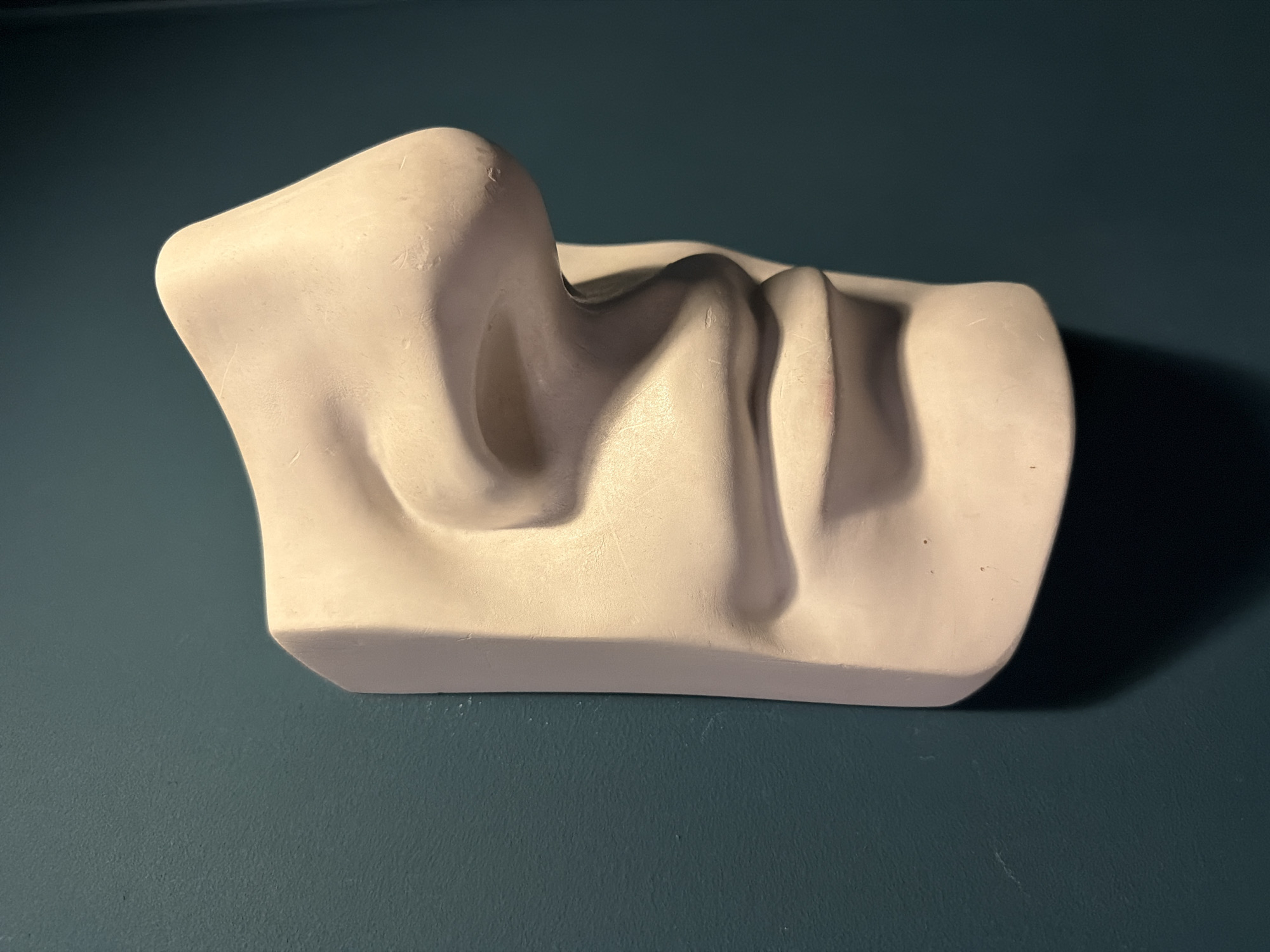 A plaster cast of a nose rests on a dark teal surface. The cast is light in color, possibly white or off-white, and depicts a partial face sculpture focusing primarily on the nose, upper lip, and surrounding areas. The surface is flat and shows slight variations in color and texture. There are no people visible in the image. The photograph is well-lit, highlighting the shape and texture of the cast. There is no evidence to suggest the image was taken in Moscow, Russia.