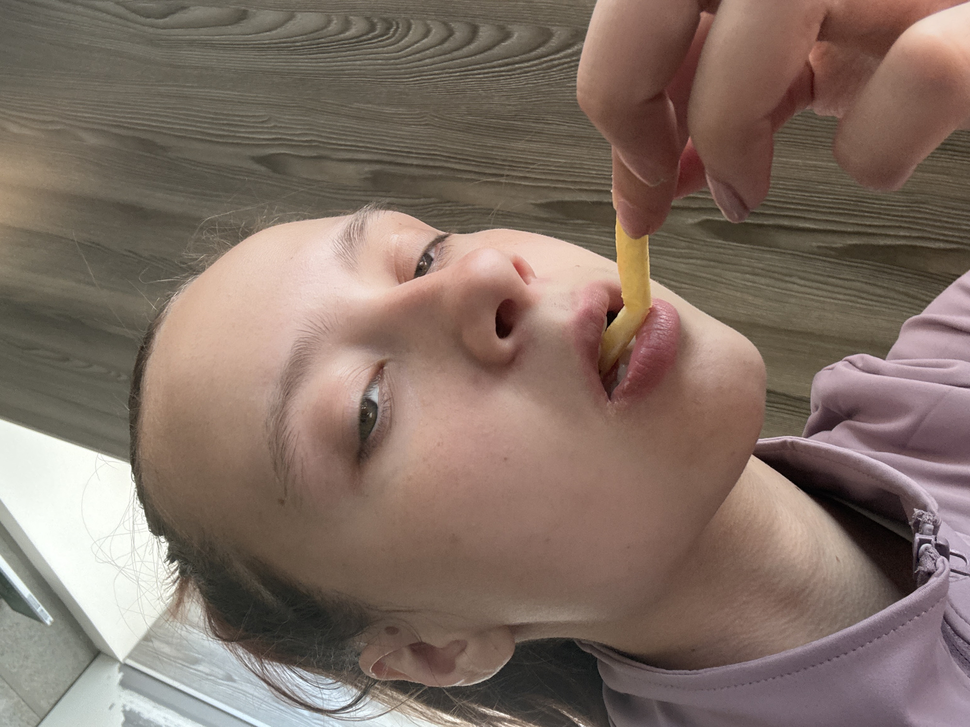 A person is holding a french fry and putting it in their mouth. The location is unknown and the query about the city of Perm, Russia cannot be confirmed from the image.