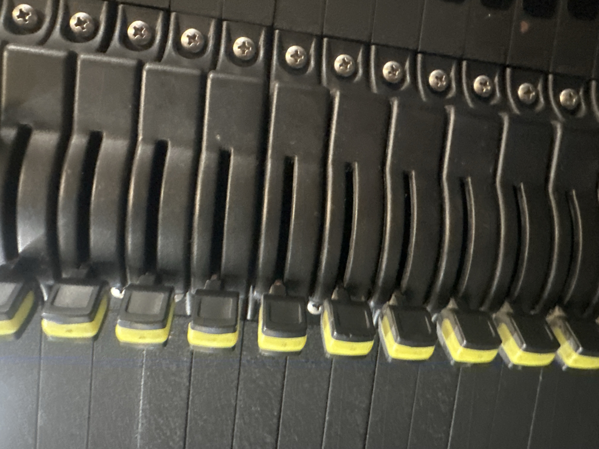 The image shows a close-up view of a row of black server hard drive bays. Each bay has a latch or lever with a yellow indicator. The levers are in the open position. The bays are secured with screws. There are no discernible people, actions, or interactions within the frame. The environment is generic and does not indicate a specific location in Tonbridge and Malling, United Kingdom.
