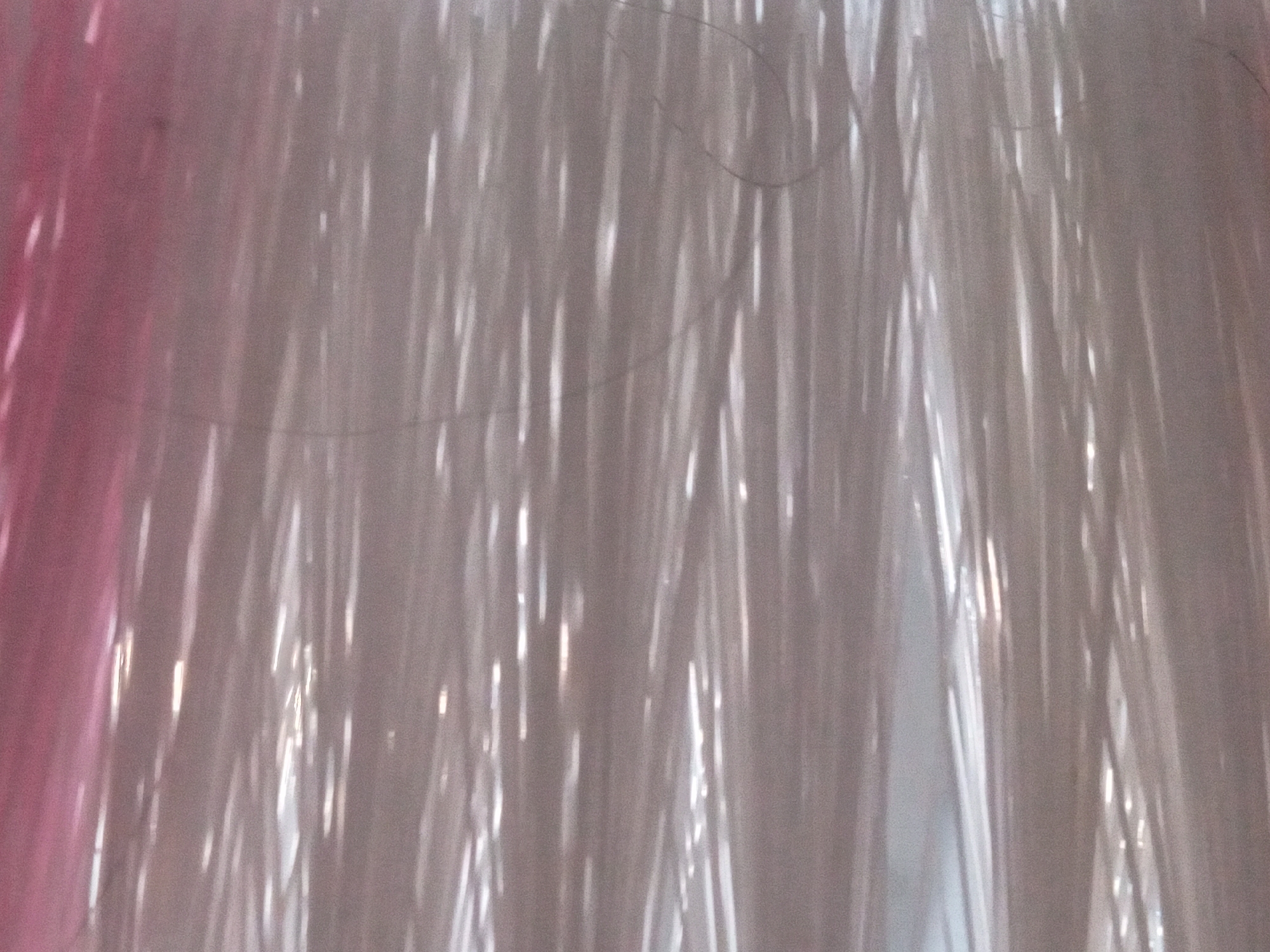 The image is an abstract close-up of a surface with pink and gray tones. There are numerous thin, bright white lines scattered across the surface, appearing as highlights or reflections. Some longer, darker, and wavy strands are also visible, suggesting fibers or hair. The overall impression is of a textured or layered material, possibly fabric or a reflective surface with embedded filaments. The lighting creates a streaky, somewhat blurred effect. The location in the city of Unknown, Unknown is irrelevant to the visual content of the image.