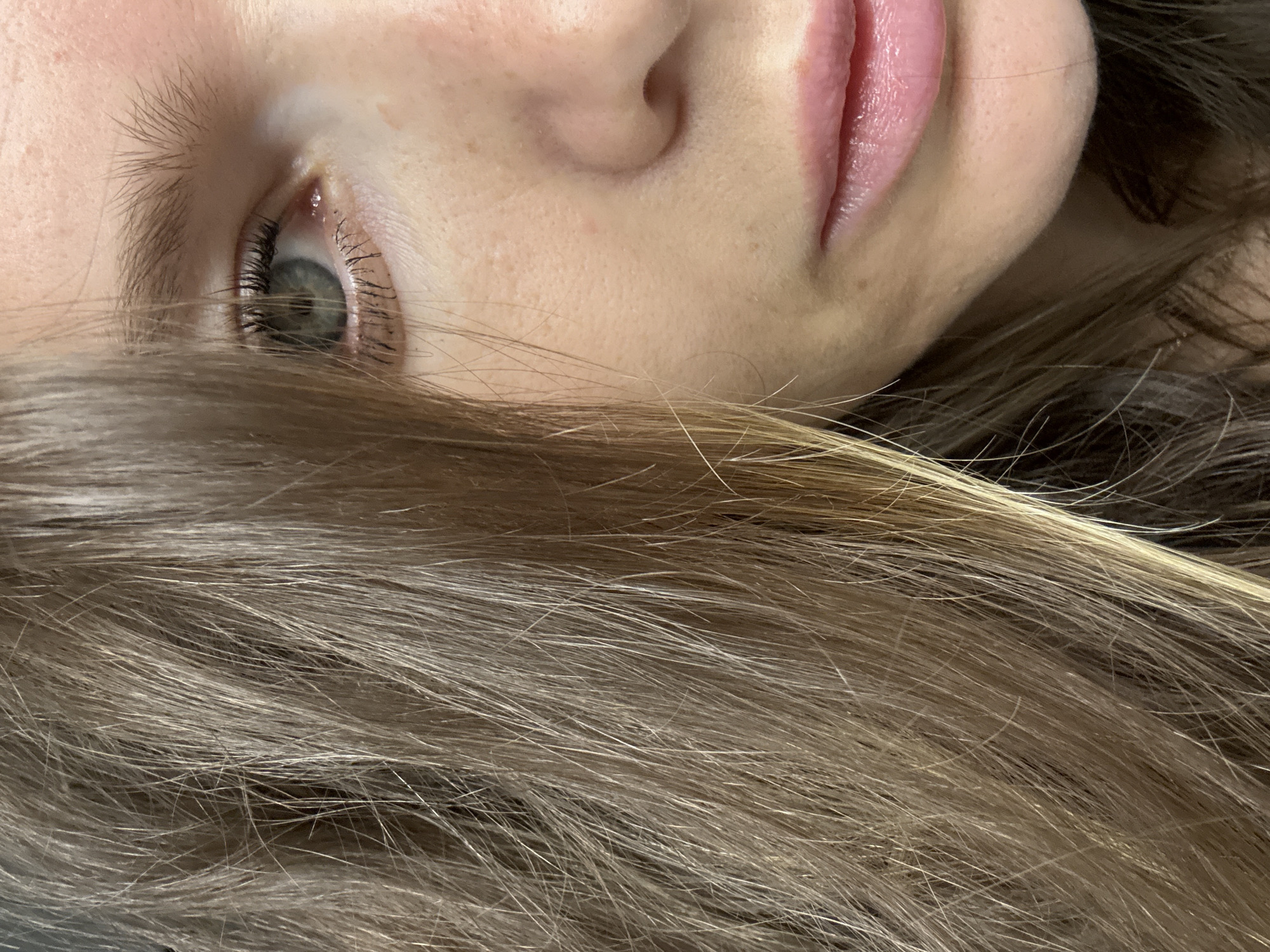 A close-up image of a person's face, tilted to the side. The person has fair skin, with freckles visible on the nose. The visible eye is gray-green. The lips are pink and appear glossy. The lower portion of the face is partially obscured by brown and blonde hair. There is no information to suggest that this image was taken in Moscow, Russia.