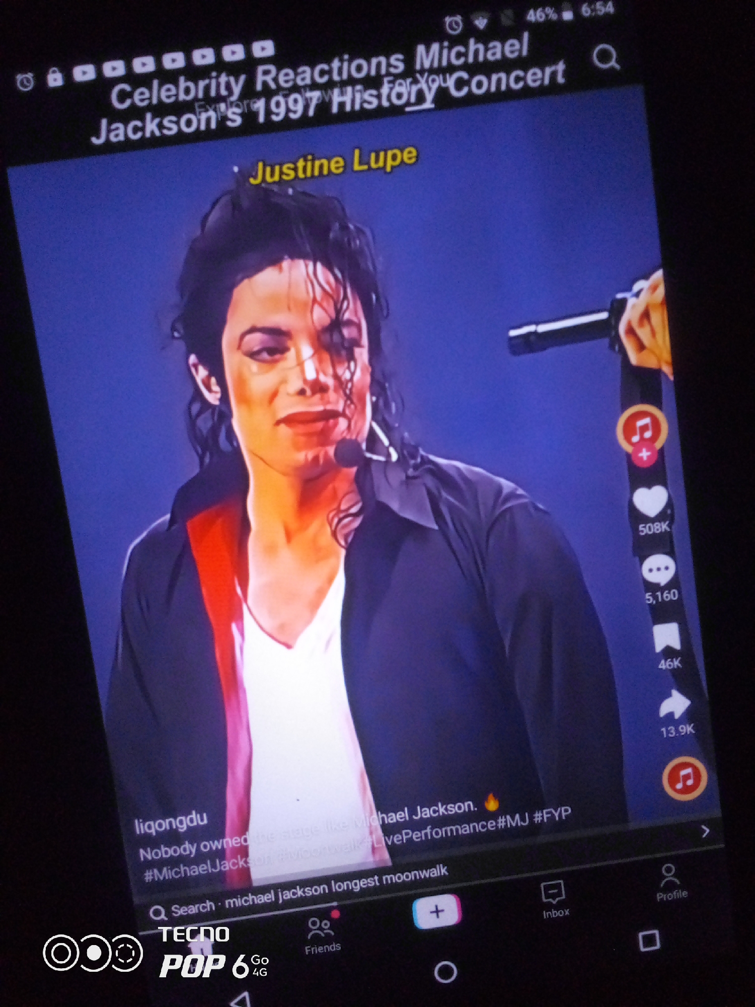 The image is a close-up of a smartphone screen displaying a TikTok video of Michael Jackson performing. The video is overlaid with text, including the title "Celebrity Reactions Michael Jackson's 1997 History Concert," and hashtags such as "#MichaelJackson," "#MJ," and "#FYP." Social media engagement metrics are visible on the right side of the screen, indicating likes, comments, and shares. The bottom of the screen shows navigation icons for a social media platform, including a search bar, a "plus" icon for creating content, an inbox, and a profile icon. The brand "TECNO POP 6 4G" is also visible at the bottom of the screen, suggesting the device is a Tecno smartphone. There is no visible indication of the city of Howayi, Nigeria, or any specific geographic location within the image.