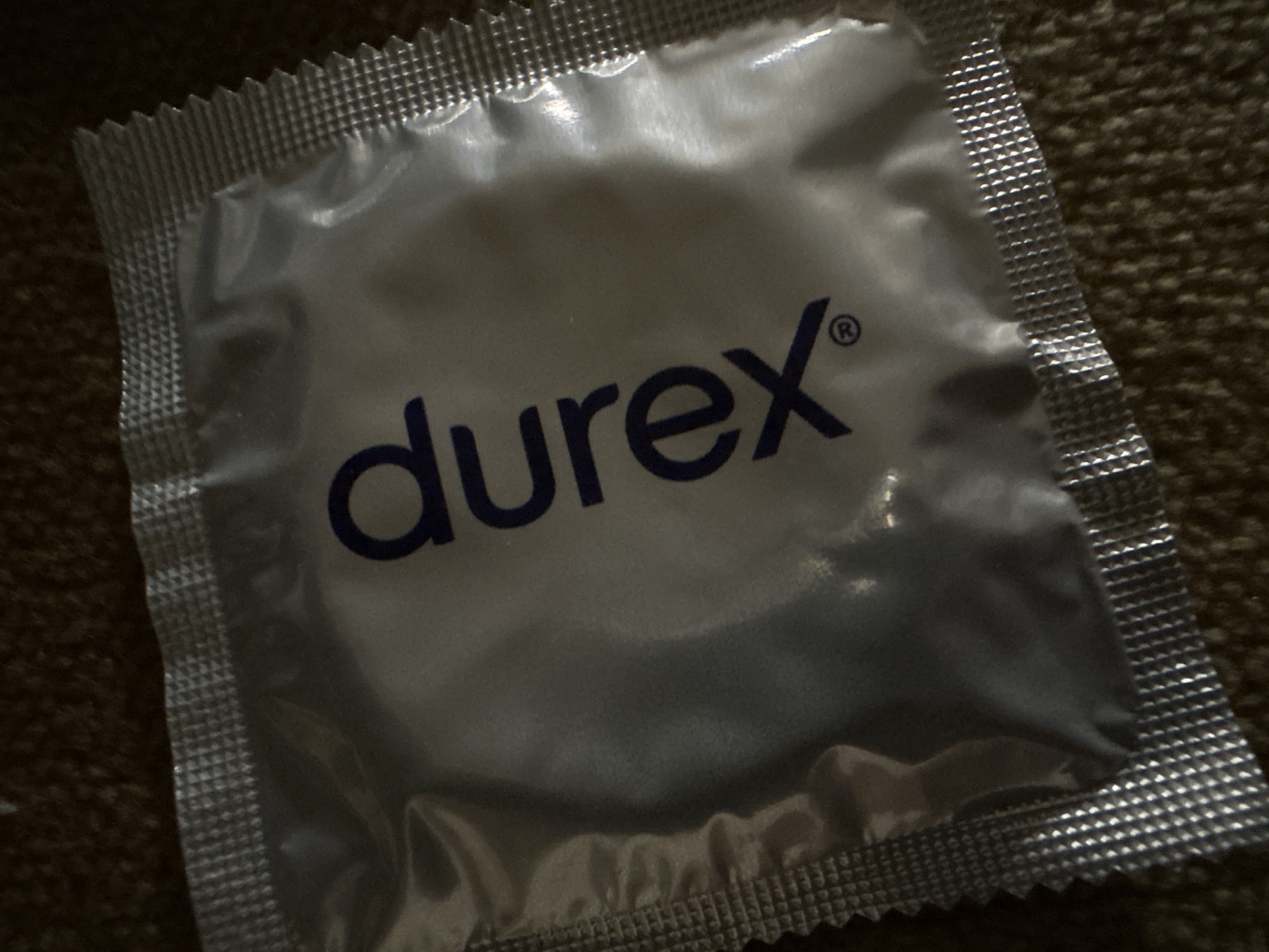 A close-up photograph shows a sealed, foil-packaged Durex condom on a textured surface, possibly fabric. The Durex logo is prominently displayed in blue on the package. The background is out of focus. There is no information to suggest that this is located in Gorna Oryahovitsa, Bulgaria.