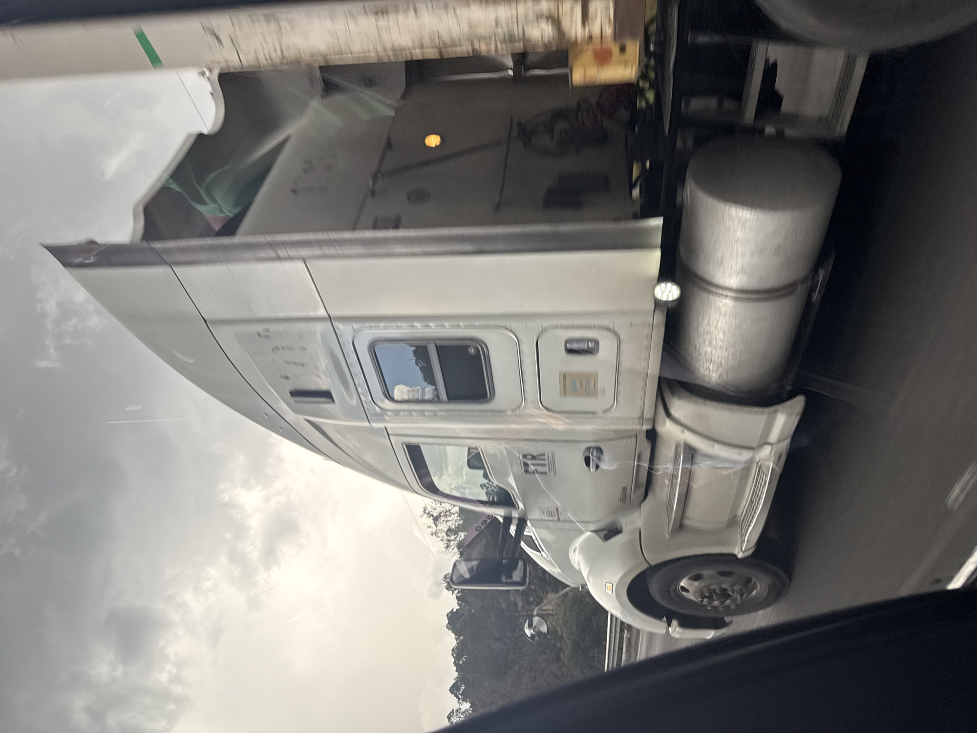 The image shows a white semi-truck on a highway. The truck has a sleeper cab and two large fuel tanks. In the background, there are trees and a cloudy sky. The location is Río Frío de Juárez, Mexico.