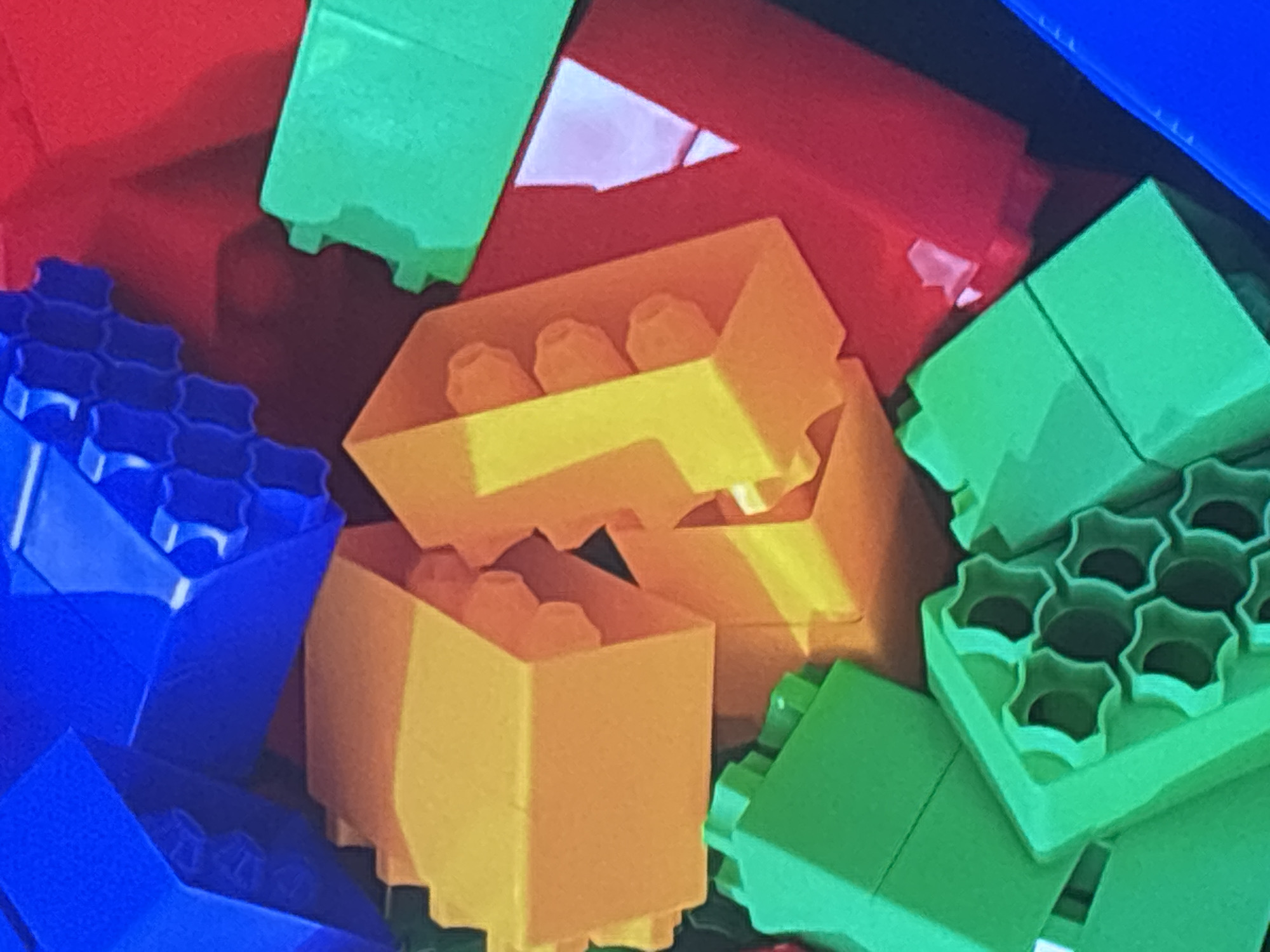 This is a close-up, overhead shot of a pile of colorful building blocks, primarily red, blue, yellow, and green. The blocks are of various shapes and sizes, including rectangular prisms and interlocking pieces. Some blocks have visible studs on top. The lighting suggests an indoor environment, likely a toy box or play area. There are no people or any discernible Dubai landmarks or context present in the image.