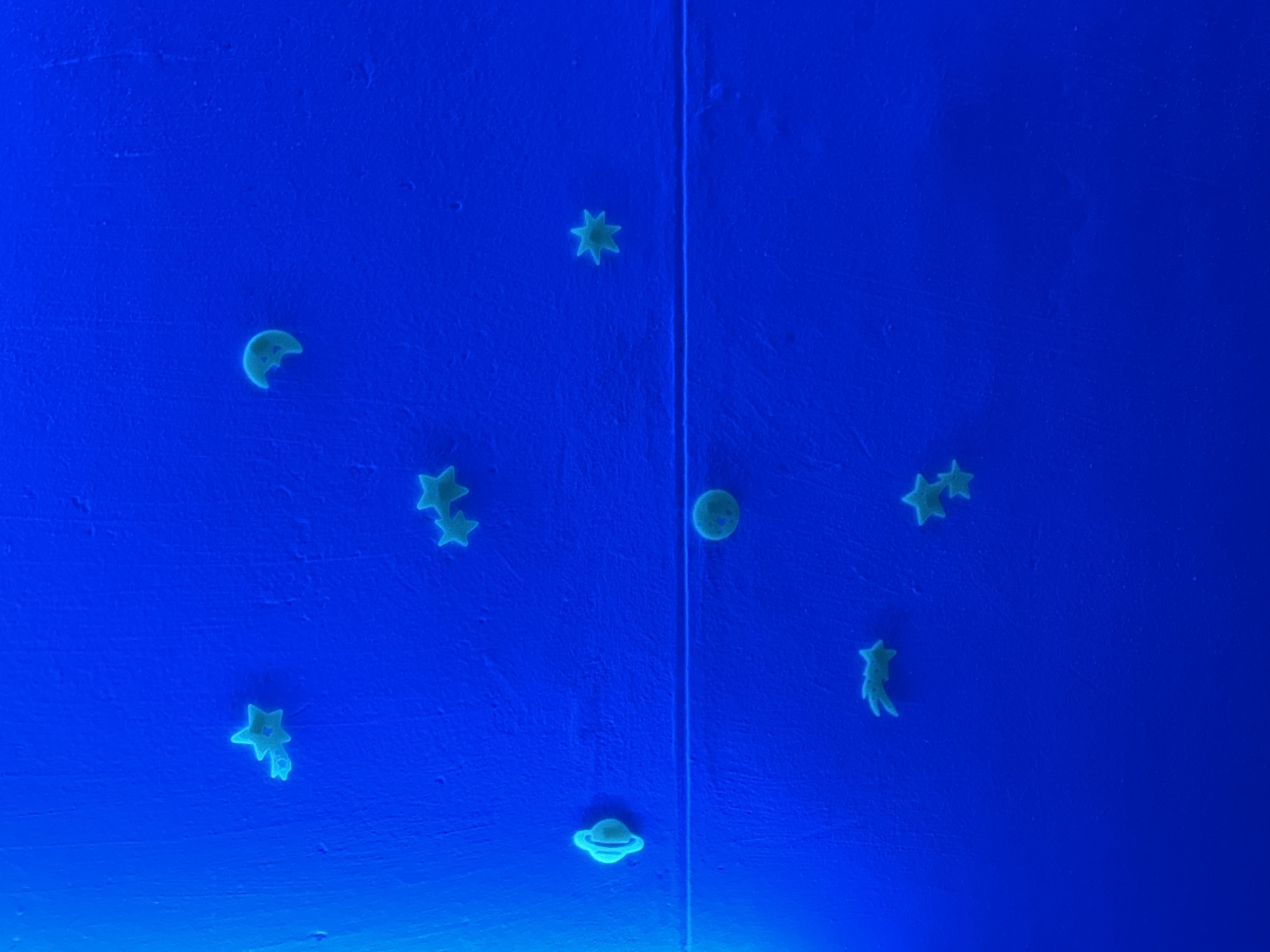 The image depicts a blue surface, potentially a wall or ceiling, adorned with glow-in-the-dark celestial shapes. These shapes include stars, a moon, a planet with rings, and a comet. The surface appears to be divided by a vertical line, possibly indicating a seam or division in the material. The location in the city of Chaikovsky, Russia, is not discernible from the image.