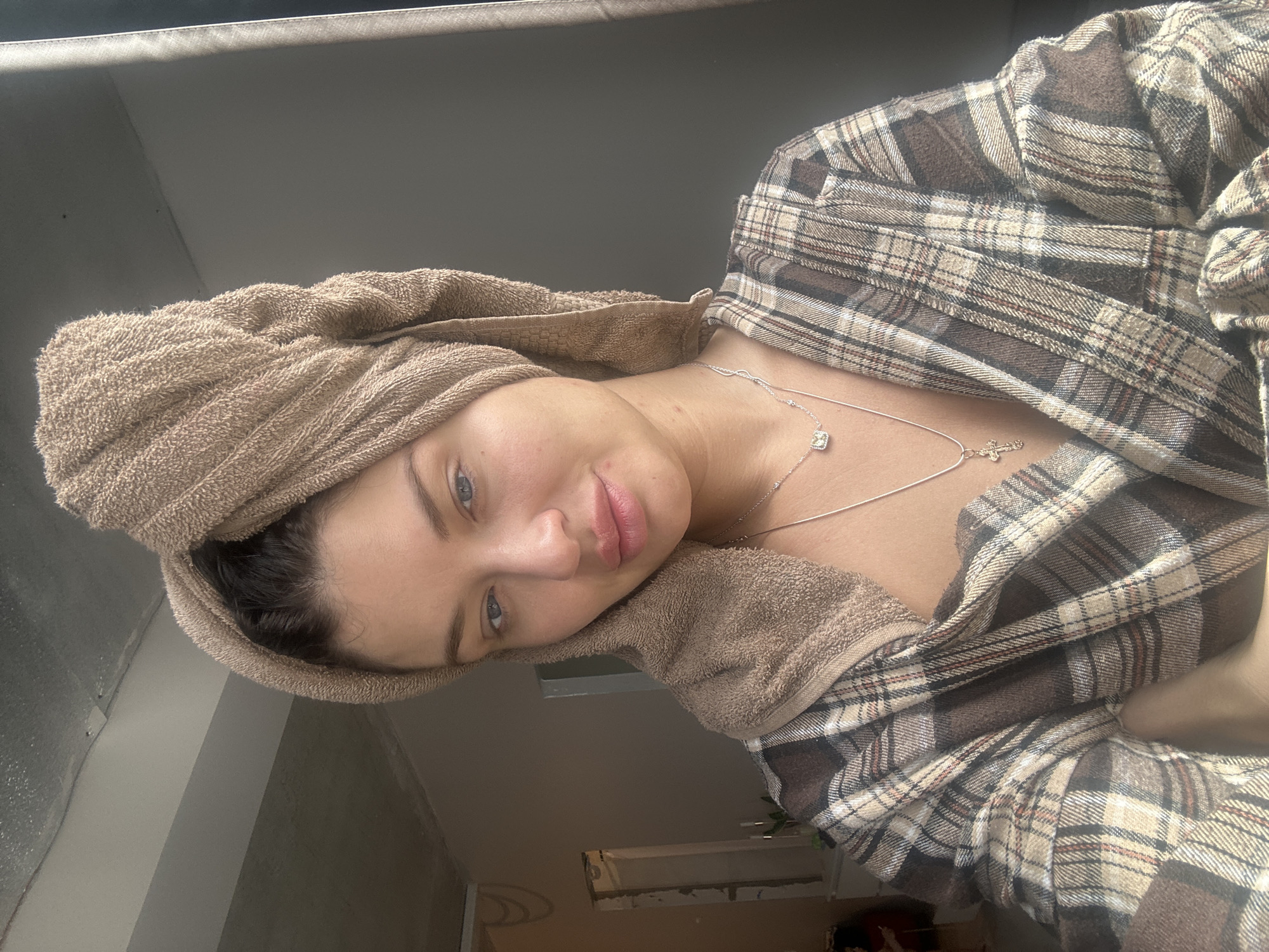 A woman with a towel wrapped around her head and wearing a plaid shirt is shown in an indoor setting. She is wearing two necklaces. The location cannot be determined to be Moscow, Russia with the given information.