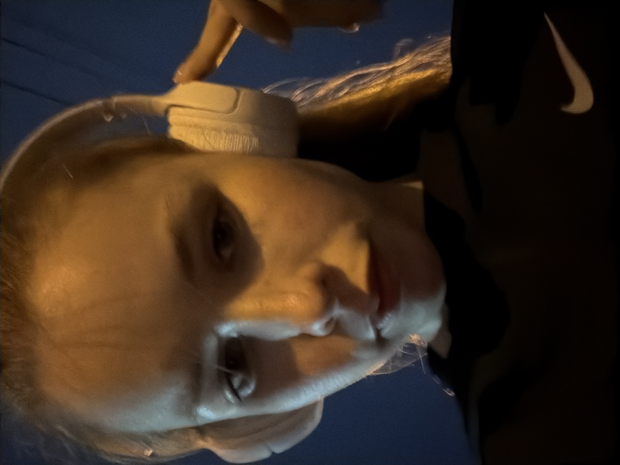 A low-angle selfie of a woman with blonde hair wearing white headphones and a dark Nike sweatshirt. The background is a dark blue, likely at night. There is no information in the image to suggest the location is Berezniki, Russia.