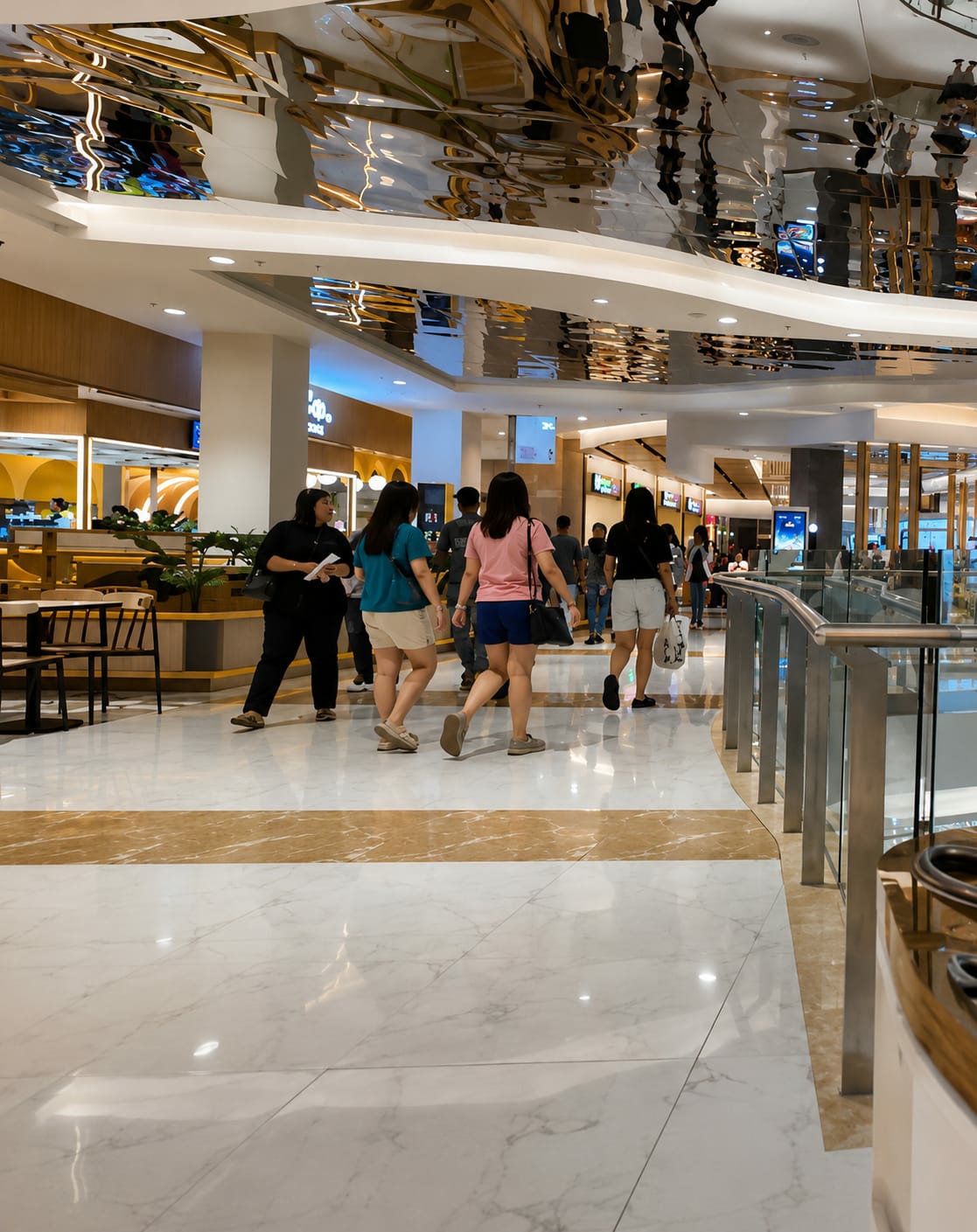 The image depicts the interior of a modern shopping mall. In the foreground, people are walking on a polished marble floor with a decorative gold inlay stripe. The ceiling is a highly reflective, curved surface, mirroring the lights and architectural features of the mall.
Several individuals are visible, mostly seen from the waist down, suggesting they are walking away from the camera. One person in a teal shirt and khaki shorts walks with another in a pink t-shirt and blue shorts. Another person in black pants and a black shirt is also visible, carrying a bag. In the background, more shoppers and mall patrons are seen, along with store fronts and displays. The overall environment is bright and airy, characteristic of a contemporary retail space.
While the specific location is not visually confirmed, the city of Medan, Indonesia, is mentioned. This suggests the scene is likely within a shopping mall in Medan, a major city known for its commercial centers. The architecture and style are consistent with malls found in urban centers across Southeast Asia.