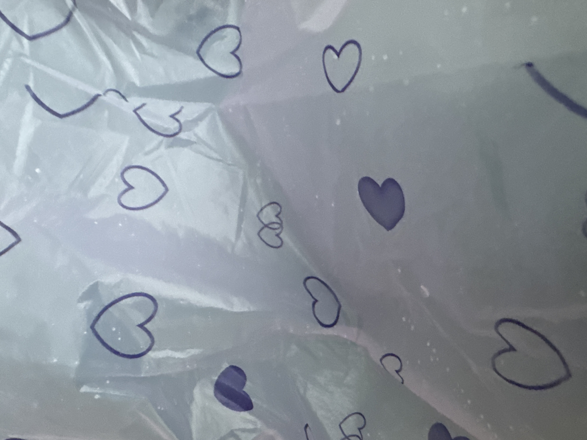 The image shows a close-up of a translucent material with a pattern of dark-blue or purple hearts on it. The material appears wrinkled and possibly plastic-like. The lighting is soft and diffused. The image was taken indoors. It is unknown if the image was taken in Lang Biang - Da Lat, Vietnam.