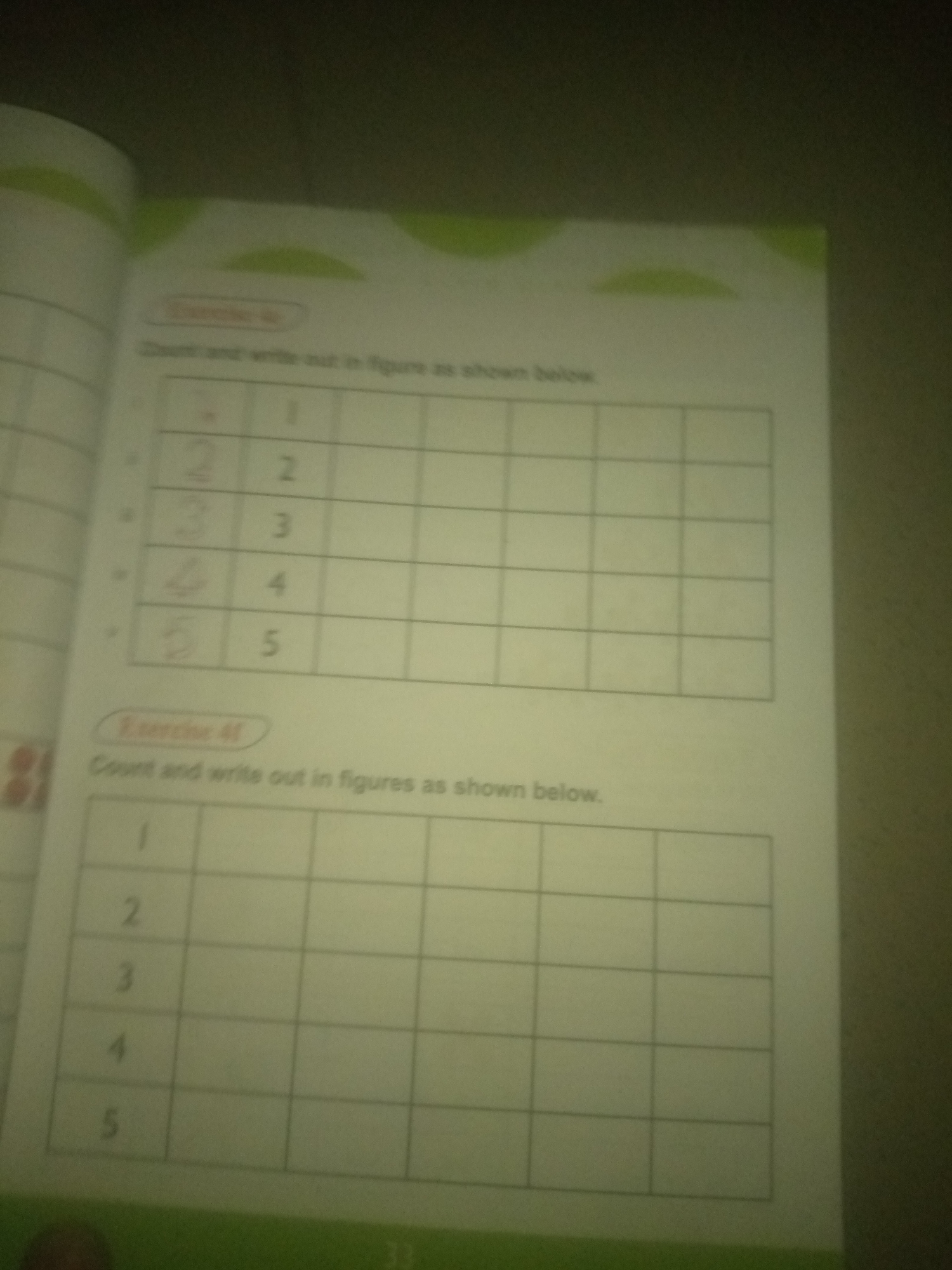 The image is a close-up, slightly blurry photograph of a page from a workbook. The page contains two exercises, labeled "Exercise 4D" and "Exercise 4E". Both exercises involve counting and writing numbers in figures as shown in a grid.
In Exercise 4D, the numbers 1 through 5 are already written in the first column of a grid. The corresponding rows have spaces for figures to be written.
Exercise 4E is similar, with numbers 1 through 5 in the first column of a grid. It also has spaces for figures to be written in the subsequent columns. The overall environment appears to be an indoor setting, likely a classroom or home, given the nature of the workbook page. There are no people or any identifiable elements of the city of Jauro Yinu, Nigeria, present in the image.