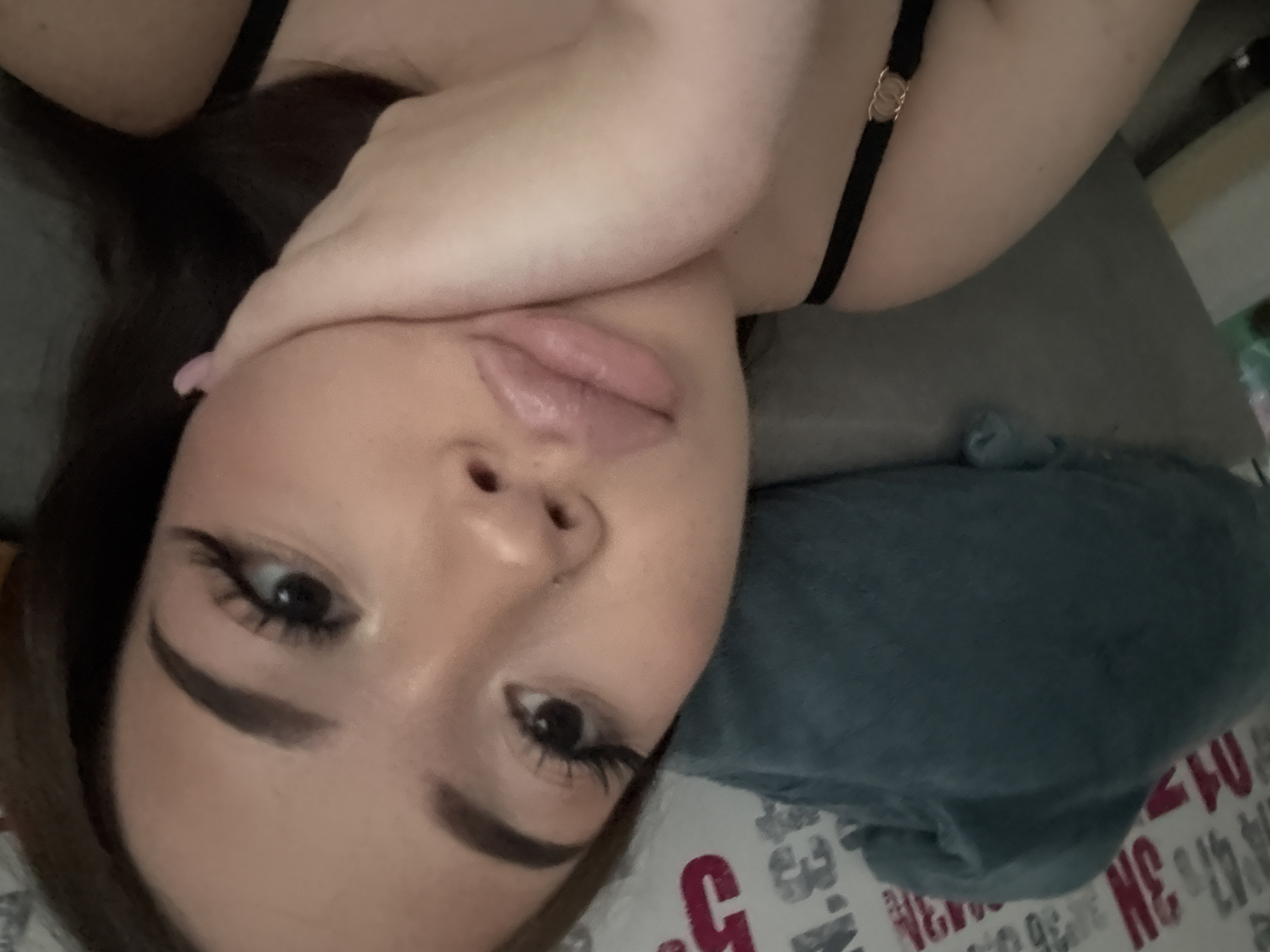 A young woman lies on her side, her head resting on her right arm. She has fair skin, brown hair, and dark eyebrows. She is wearing heavy eye makeup. Her lips are full and pink. She is wearing a black top with gold embellishments. She is lying on a bed with a blue pillow and patterned sheets.
There is no information to suggest this image was taken in Naberezhnye Chelny, Russia.