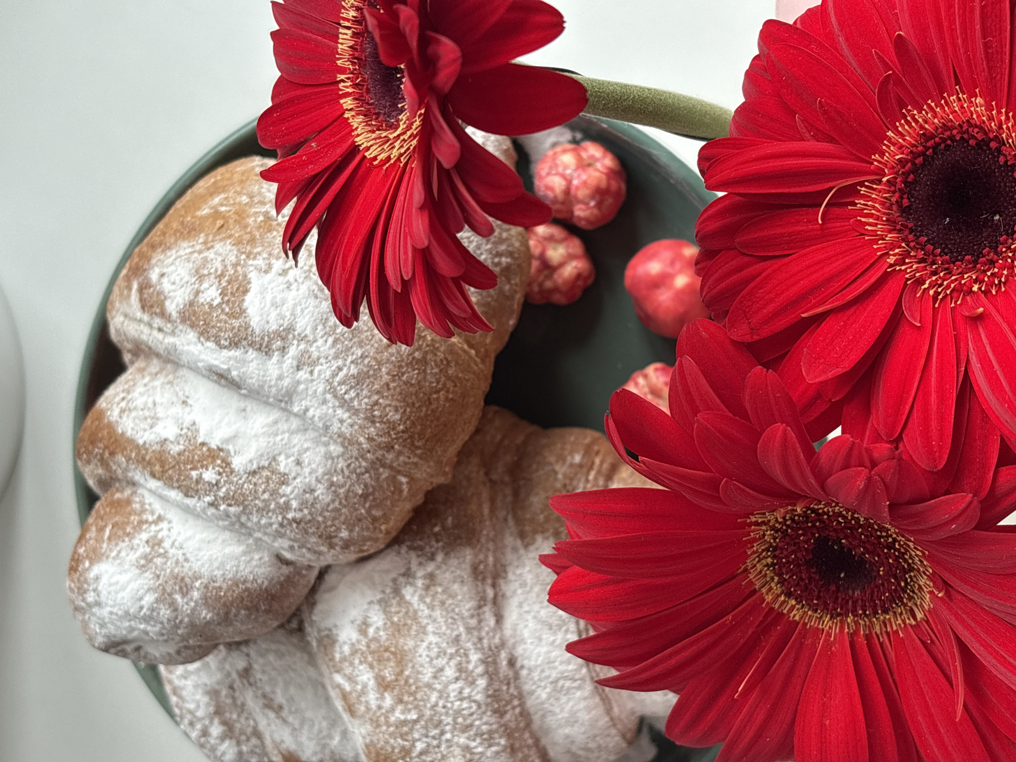 A close-up shot depicts a plate containing pastries dusted with powdered sugar, interspersed with red gerbera daisies and small, decorative red and beige spheres. The scene is set against a white surface. The location and specific details relating to the city of Chaikovsky, Russia, are not discernible within this image.
