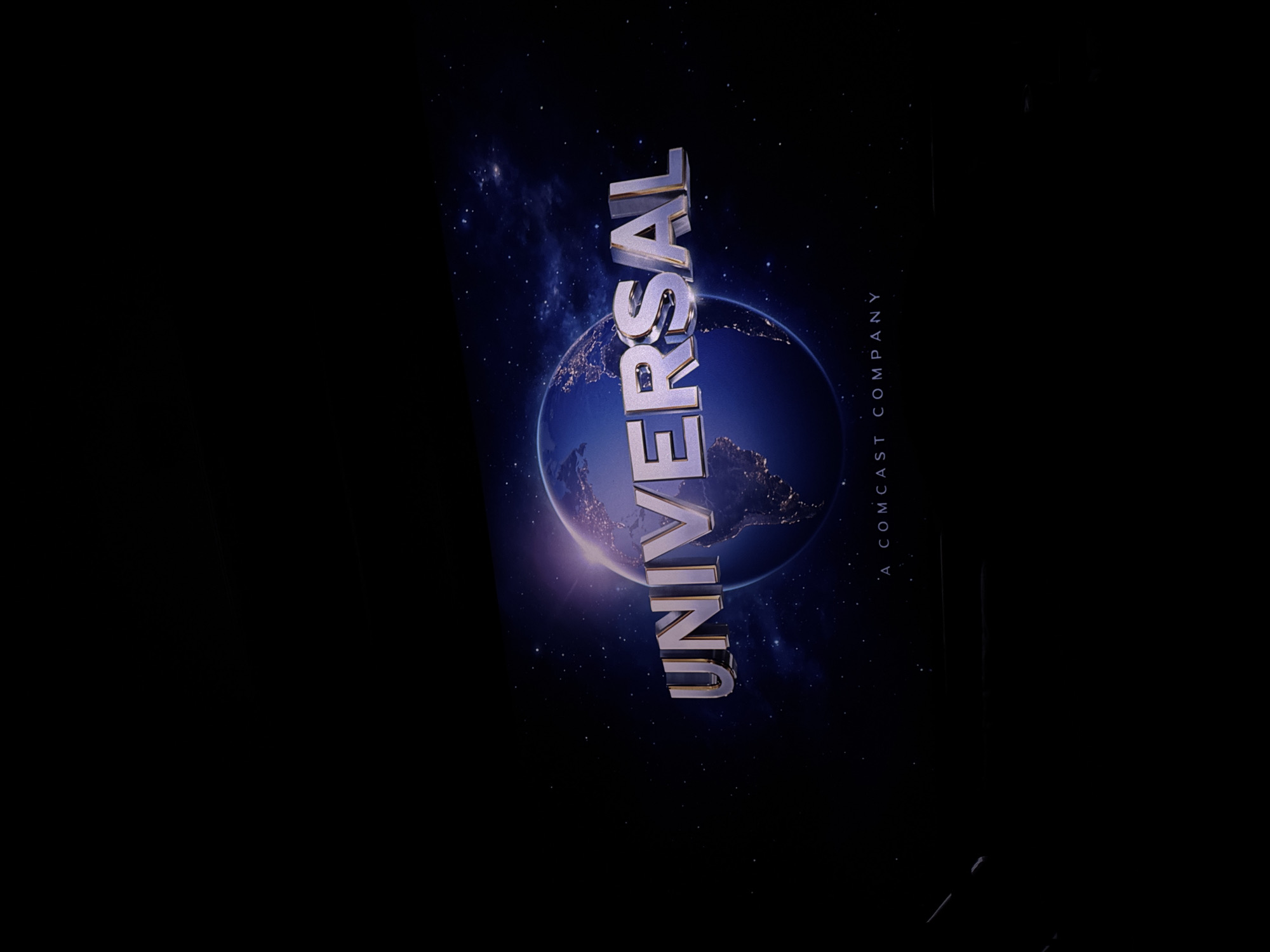 The image depicts the Universal Pictures logo against a backdrop of Earth in space. The text "UNIVERSAL" is rendered in three-dimensional, metallic lettering. Below and to the right is the text "A COMCAST COMPANY." The location of Puebla, Mexico is not apparent.