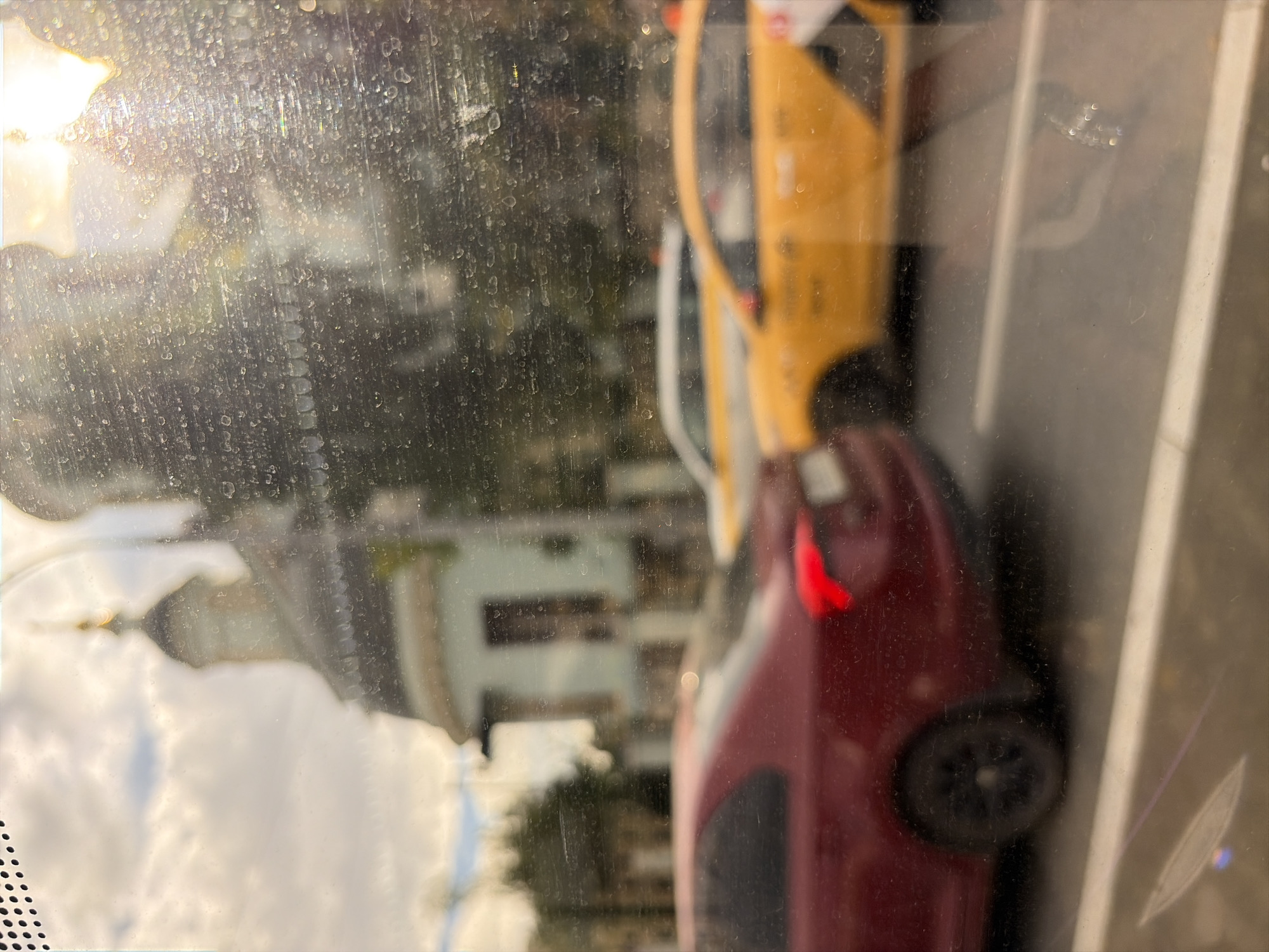 The image, taken through a dirty window, shows a blurred street scene with several cars. A red sedan is in the foreground on the left. To its right, two yellow taxis are driving in traffic. In the background, a light blue building with brown windows and a domed roof, possibly a church, is visible. The sky is cloudy with bright sunlight shining through. The location is identified as Moscow, Russia.
