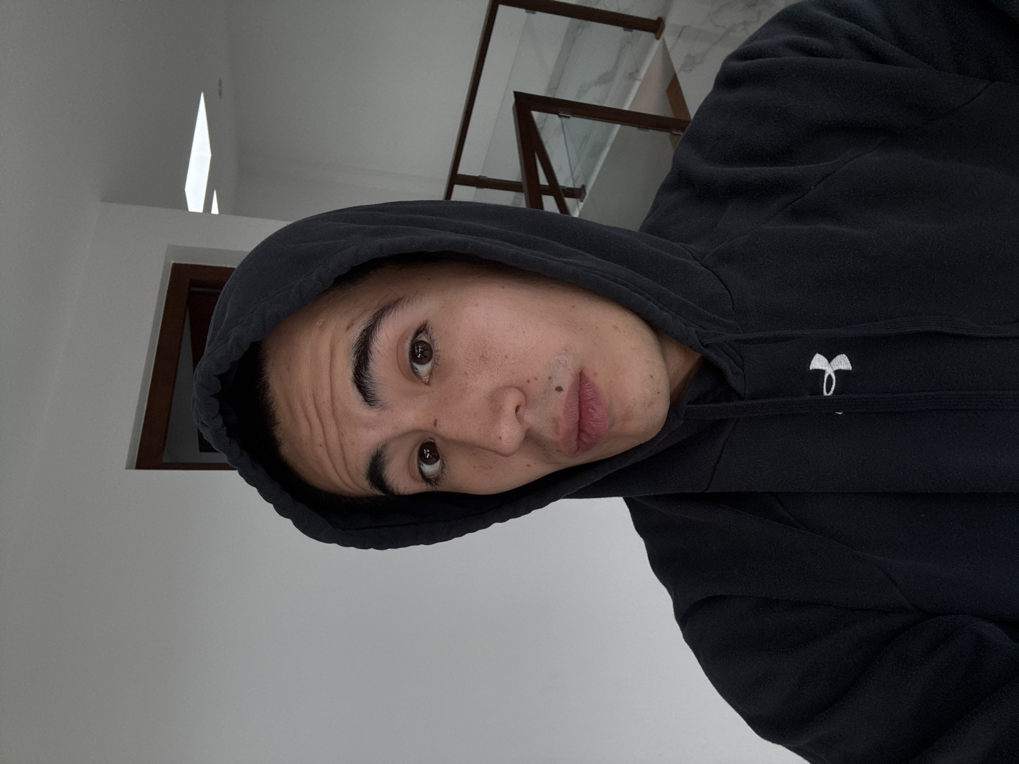 A person wearing a black hooded sweatshirt is positioned in front of a white wall and a doorway. A railing is partially visible in the background. No information is available to definitively place the scene in San Bernardino Tlaxcalancingo, Mexico.