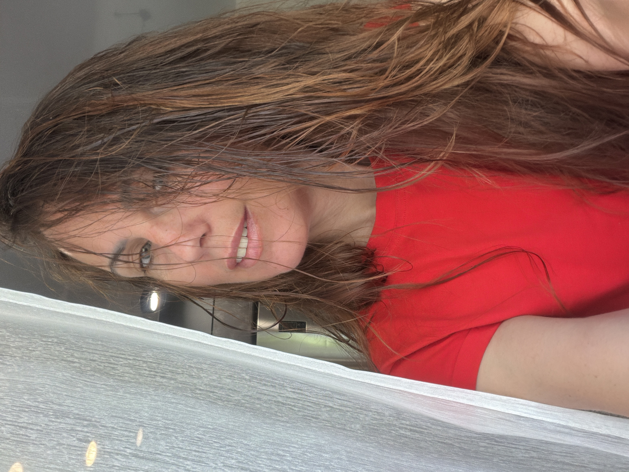 A woman with long, wet, brown hair, wearing a red shirt, lies on a white fabric surface. The location is unknown and cannot be determined to be Birobidzhan, Russia based on the visual information provided.