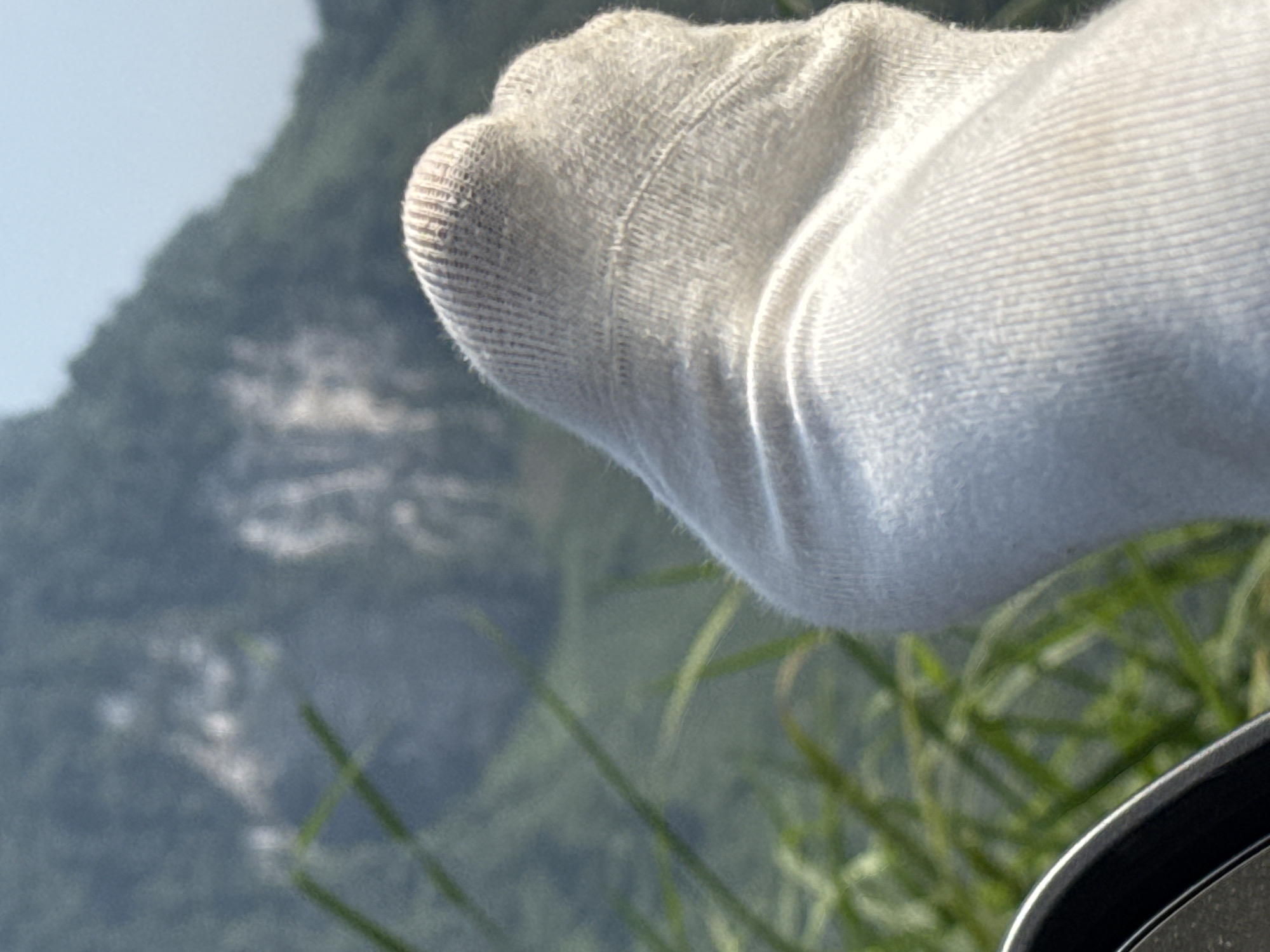 The image shows a foot in a white sock resting on a car window. The background features out-of-focus grass, trees, and a mountain. The location is Đường Thượng Commune, Vietnam.