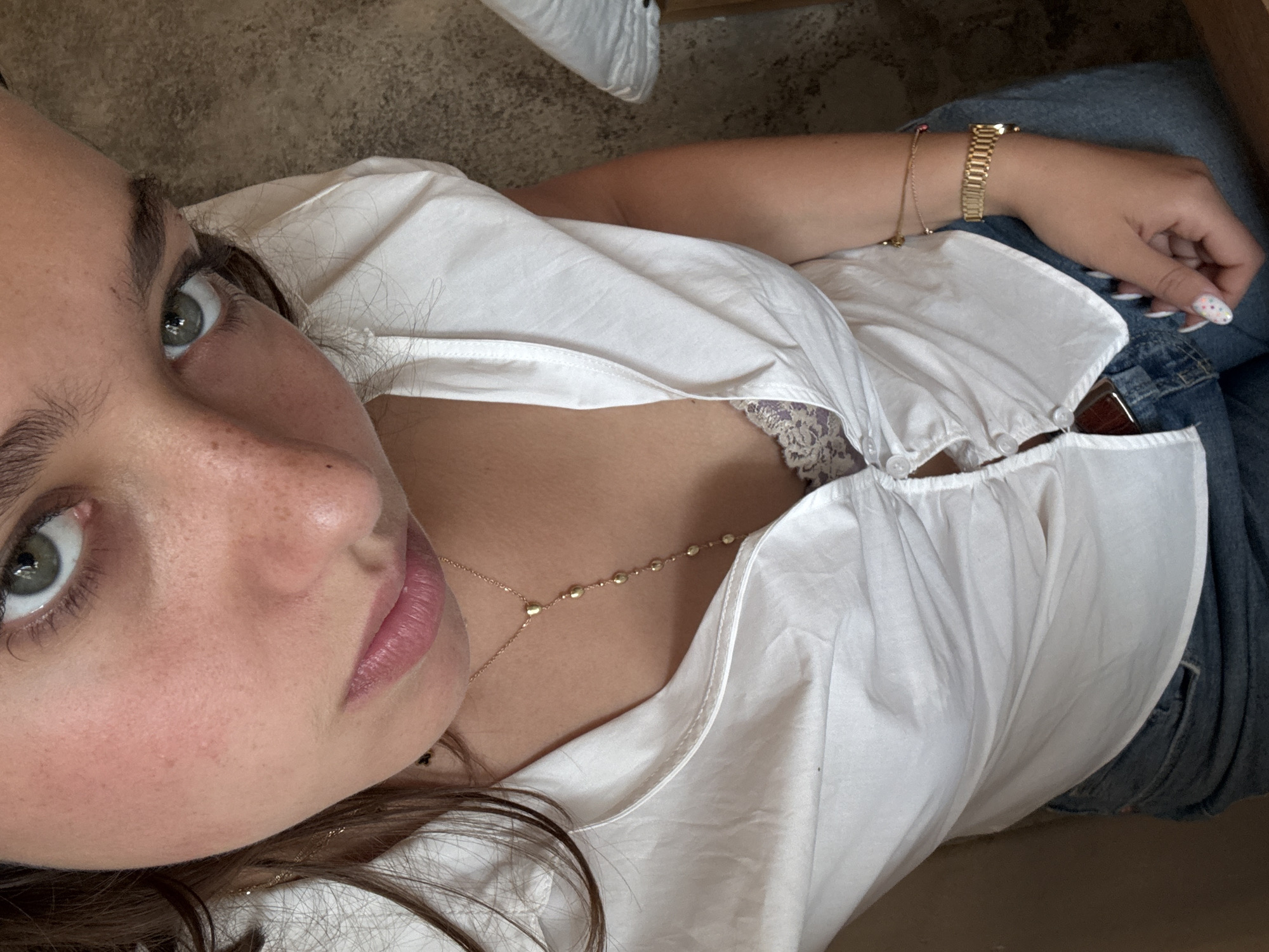 A close-up, eye-level shot of a woman wearing a white blouse, jeans, a gold necklace, and a gold watch. The scene appears to be indoors. No specific landmarks or details are present to indicate a precise location in Sofia, Bulgaria.
