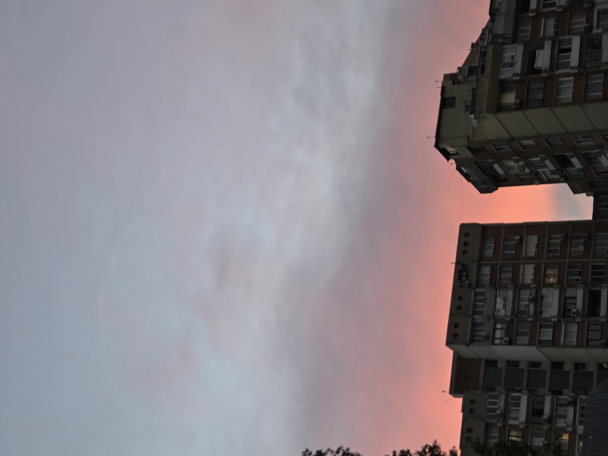 The image, rotated, shows two high-rise buildings against a twilight sky of pink and grey hues. The buildings are boxy and appear to be from the mid-20th century, with multiple rectangular windows. The sky indicates a time near sunset or sunrise. The location appears to be in Varna, Bulgaria.