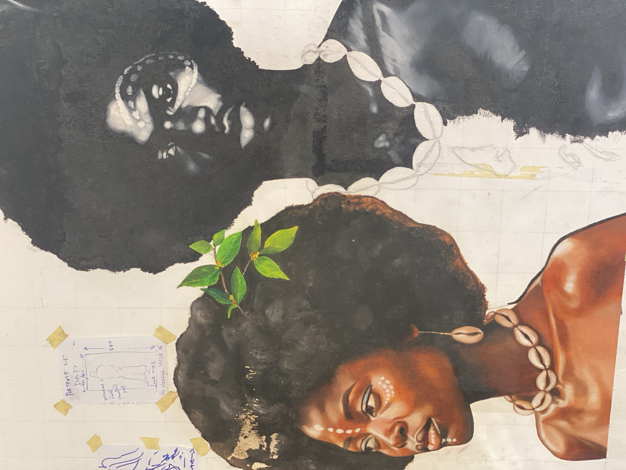 The image is a close-up shot of an in-progress painting on a canvas. The canvas is marked with a grid pattern and has notes and sketches taped to it. The painting depicts two Black women lying on their sides. One is fully rendered in warm browns and has an afro with a sprig of leaves tucked into it, as well as tribal markings painted on her face and a necklace of cowrie shells. The other woman above is unfinished, painted in grayscale with the same cowrie shell necklace. The painting gives the impression that it takes place in Ado, Nigeria.