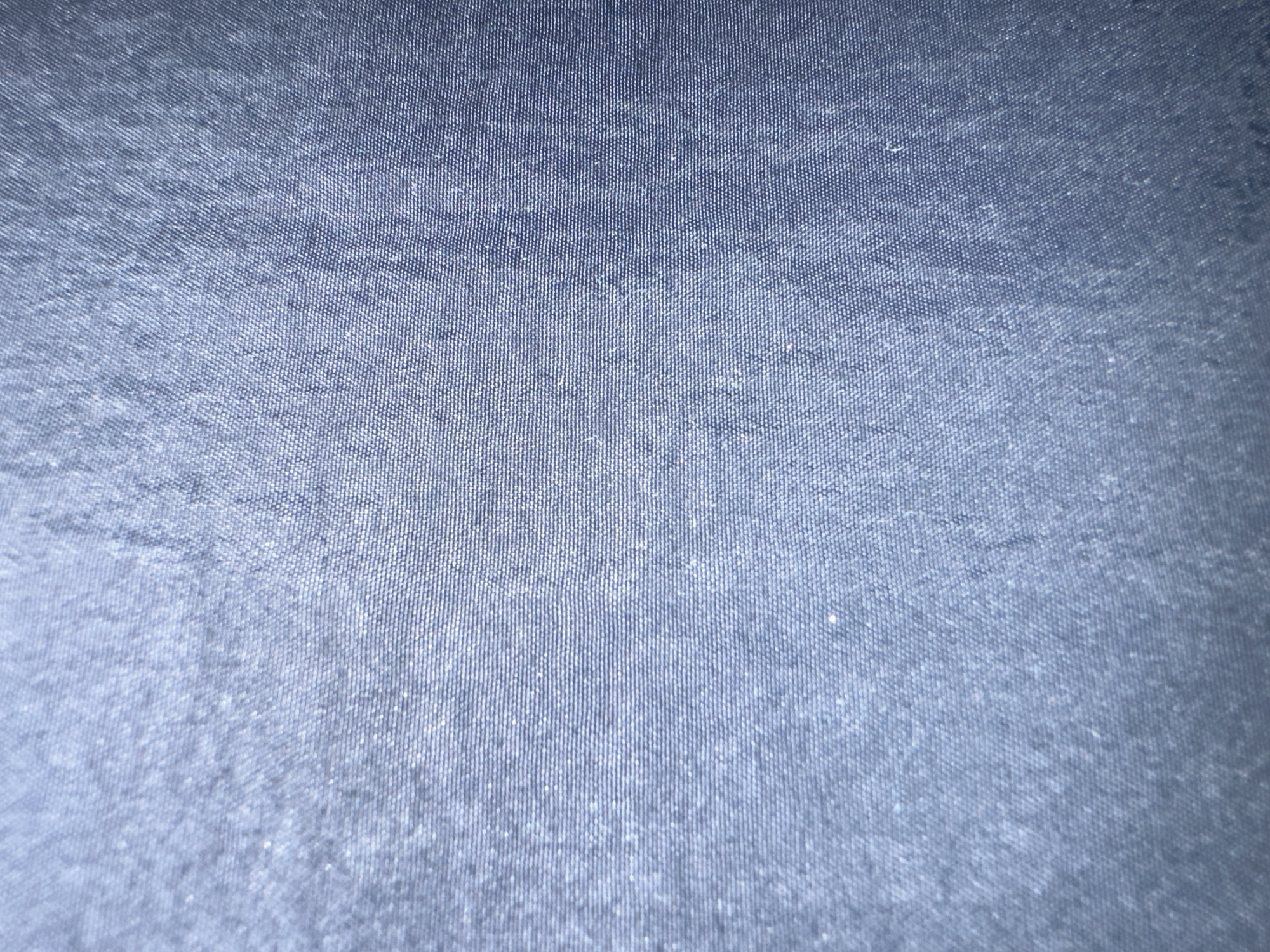 The image displays a close-up view of blue fabric with a textured weave, likely denim or a similar material. The lighting creates a slightly gradient effect, with the top left appearing brighter and the bottom right darker. The fabric exhibits a subtle pattern of horizontal and vertical threads. There are no identifiable features of Letterkenny, Ireland, or any people or actions present in the image.