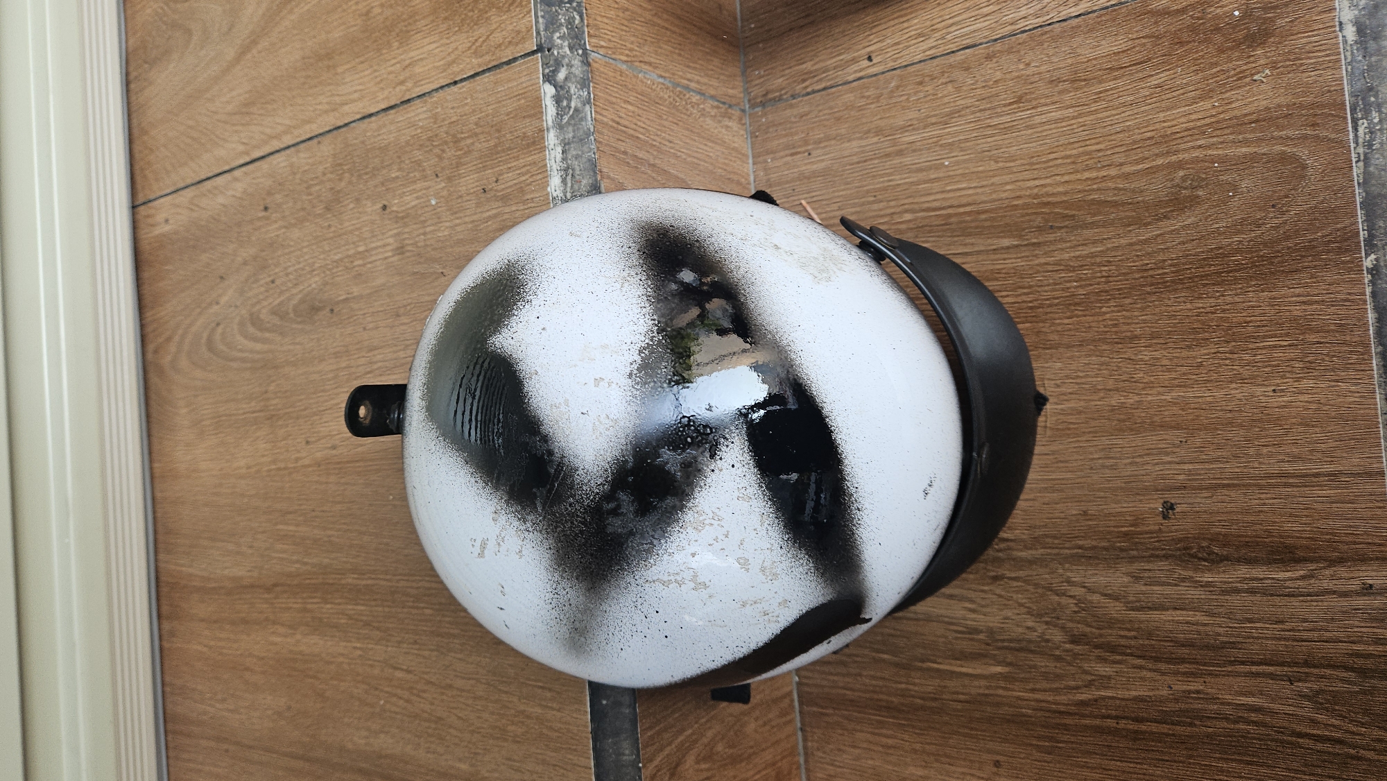 A white, round object, possibly a helmet, with black markings is lying on a wooden surface. The markings appear to be spray-painted. The surface has the appearance of wooden planks or laminate flooring. There's a gray metallic bar next to the round object and part of a white wall with vertical grooves on the far left side. The image was taken in Nha Trang, Vietnam.