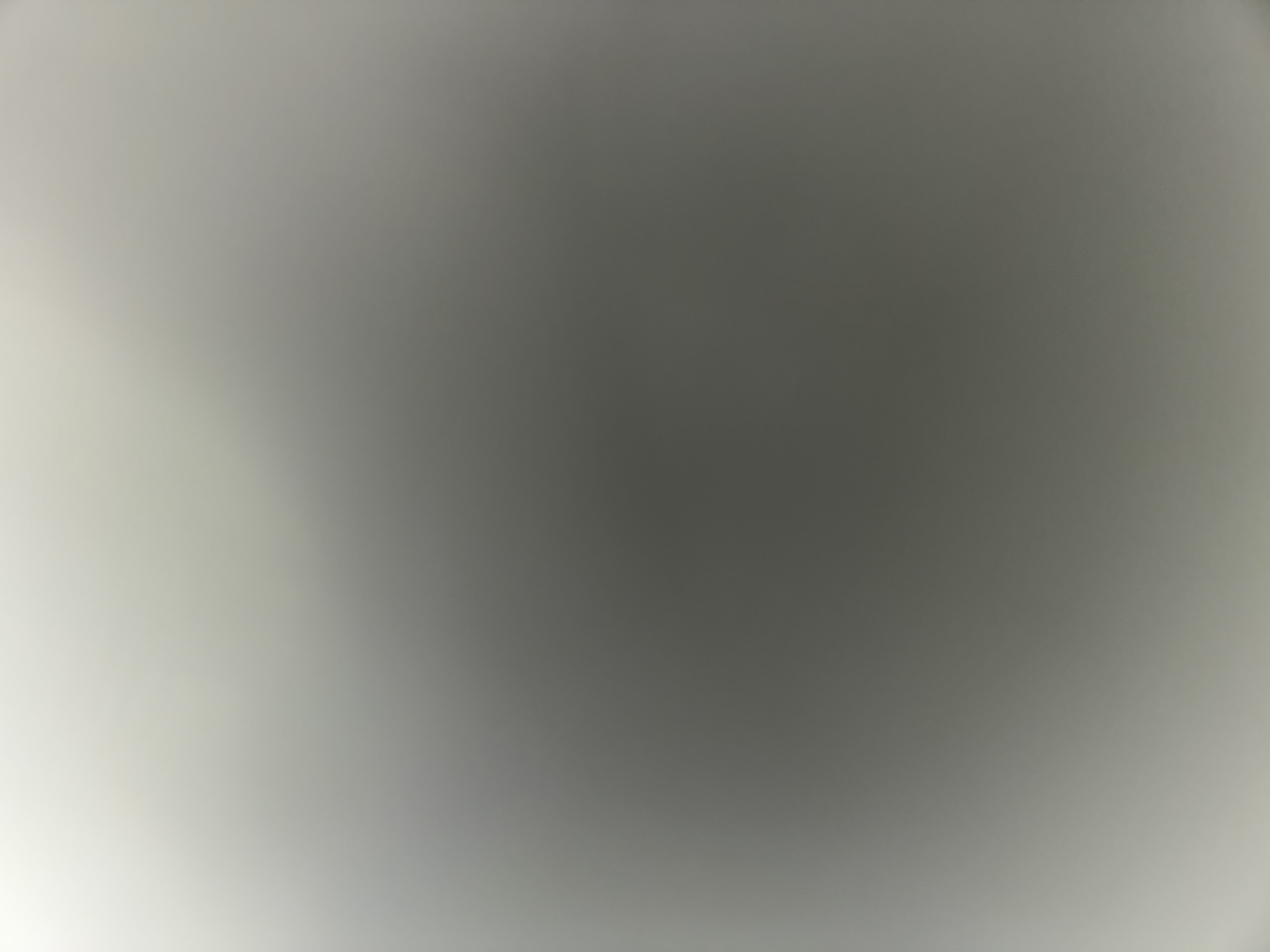 The image is an abstract, out-of-focus, and brightly lit scene with a gradient of light and shadow. The colors are predominantly light grey, transitioning to a darker grey in the center and then back to a lighter grey at the bottom and top edges. There are no discernible subjects, objects, or details that can be identified to describe a scene in Navbahor, Uzbekistan, or any specific location. The image lacks any context or identifiable features.