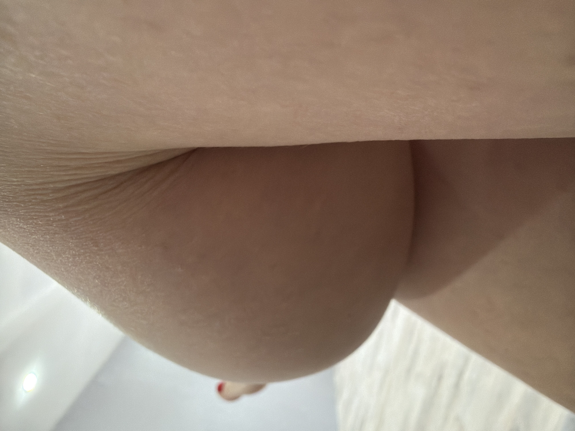 The image shows a close-up, low-angle view of human skin. The scene is indoors, with a white or light-colored floor visible in the background. The skin appears smooth. A small glimpse of what appears to be a toe with red nail polish is visible in the lower left. The setting in Chaikovsky, Russia is not supported by any detail in the image.